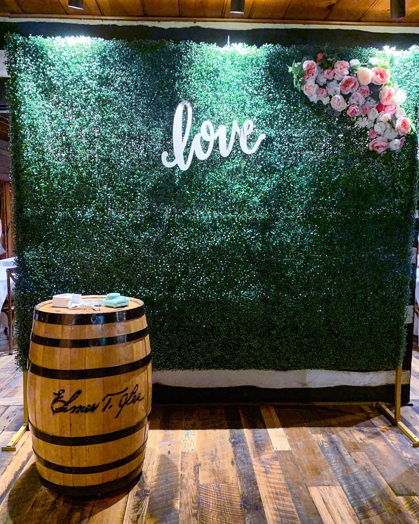 Large boxwood greenery wall accented by a bourbon barrel and Love sign