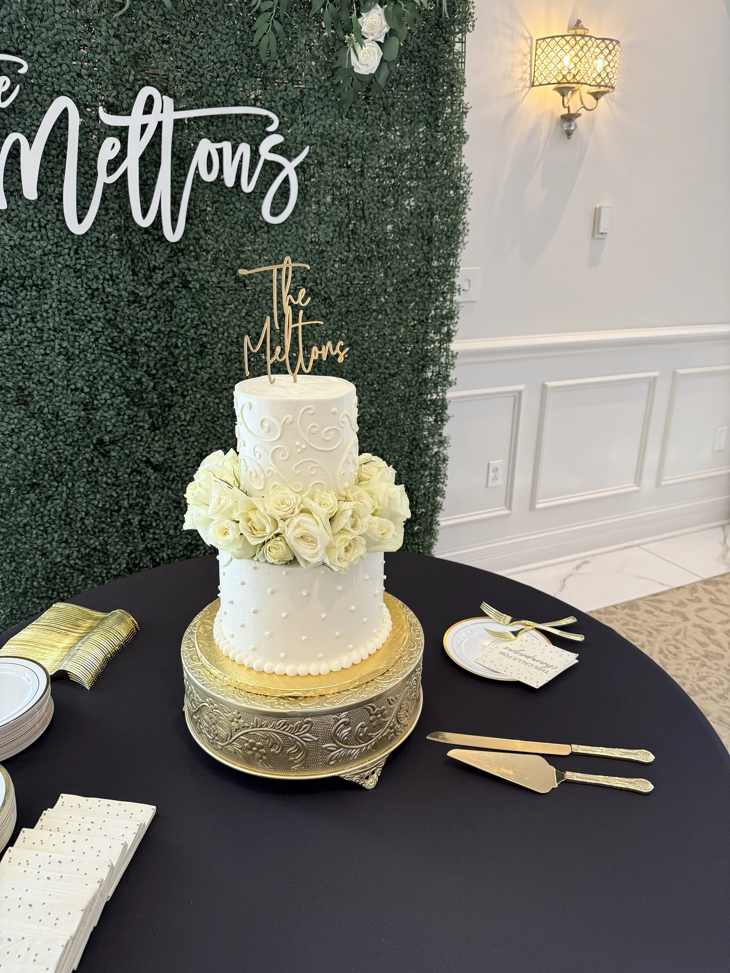 Two tiered white wedding cake decorated with white roses on a gold cake stand from Rustic and More- Lexington KY Event Rentals.