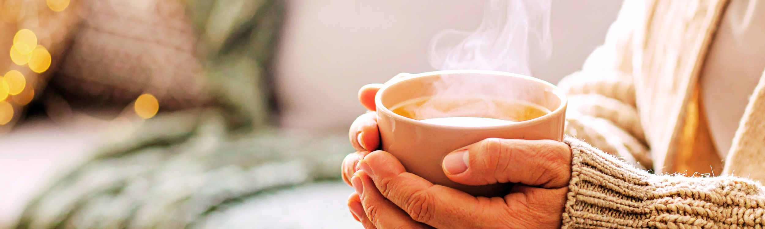 Cozy morning scene with hands holding a steaming mug of tea, wearing a soft sweater, symbolizing calm routines and mindful living.