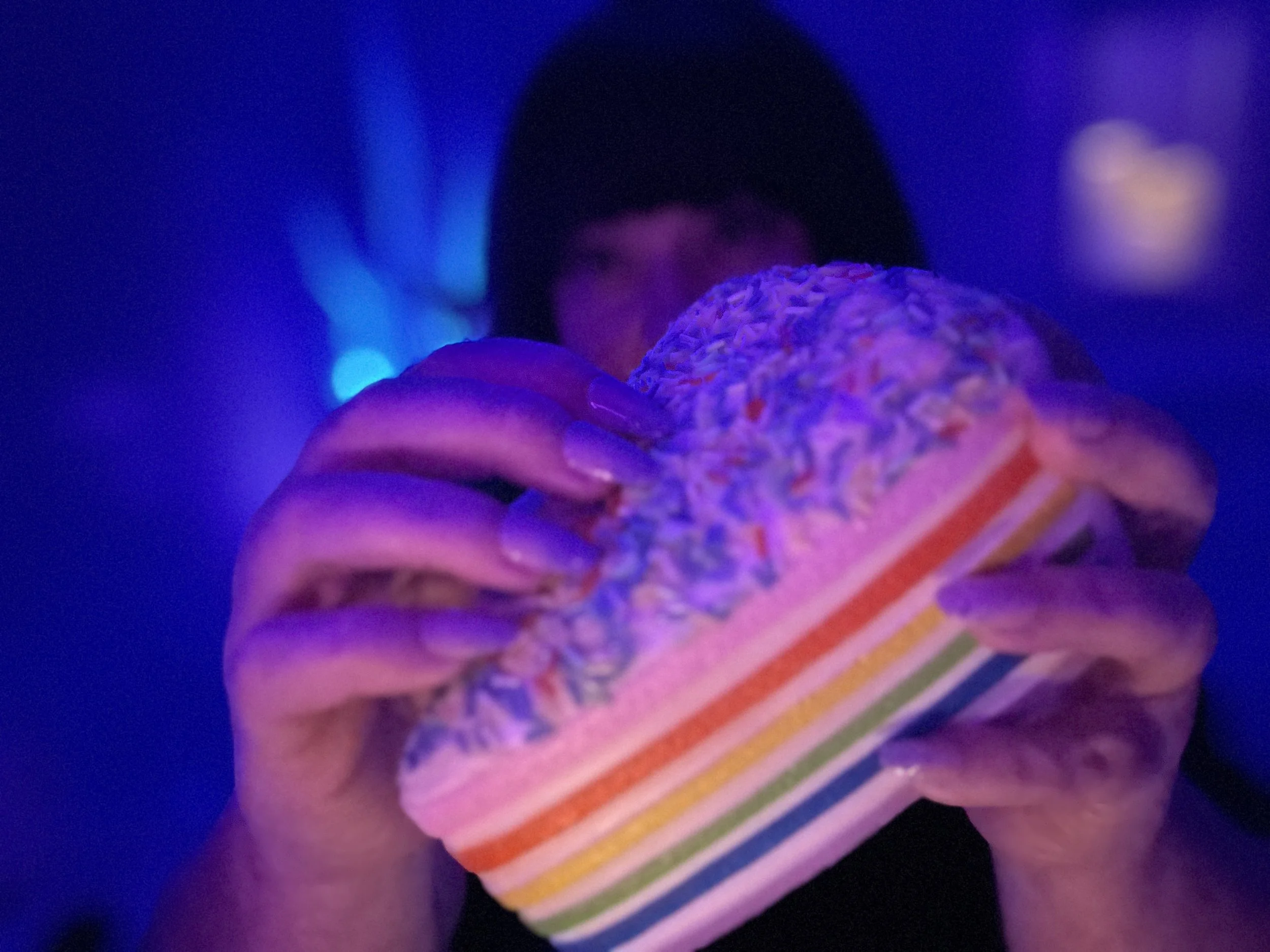 Woman holding and gently tapping a colorful rainbow sprinkle squishy cake in a calming purple-lit ASMR setting, creating relaxing tapping and scratching sounds for sleep and stress relief.