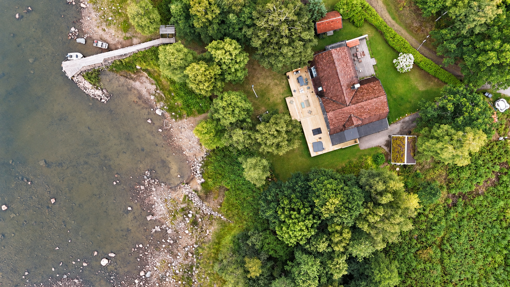 Flygbild över The Villa, terrassen vid sjön, trädgården och bryggan vid sjön Åsunden