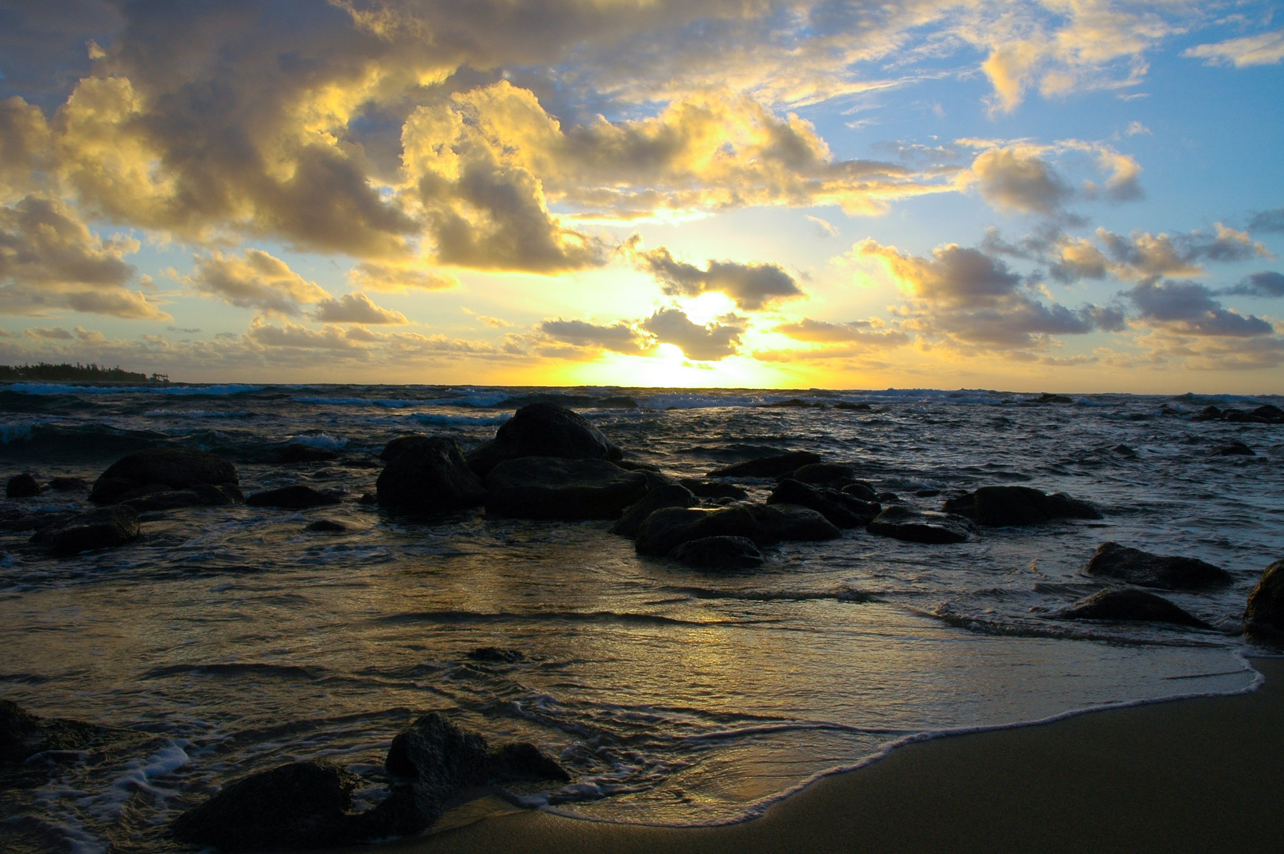 Sunset over the ocean with rocks in the water and clouds in the sky.