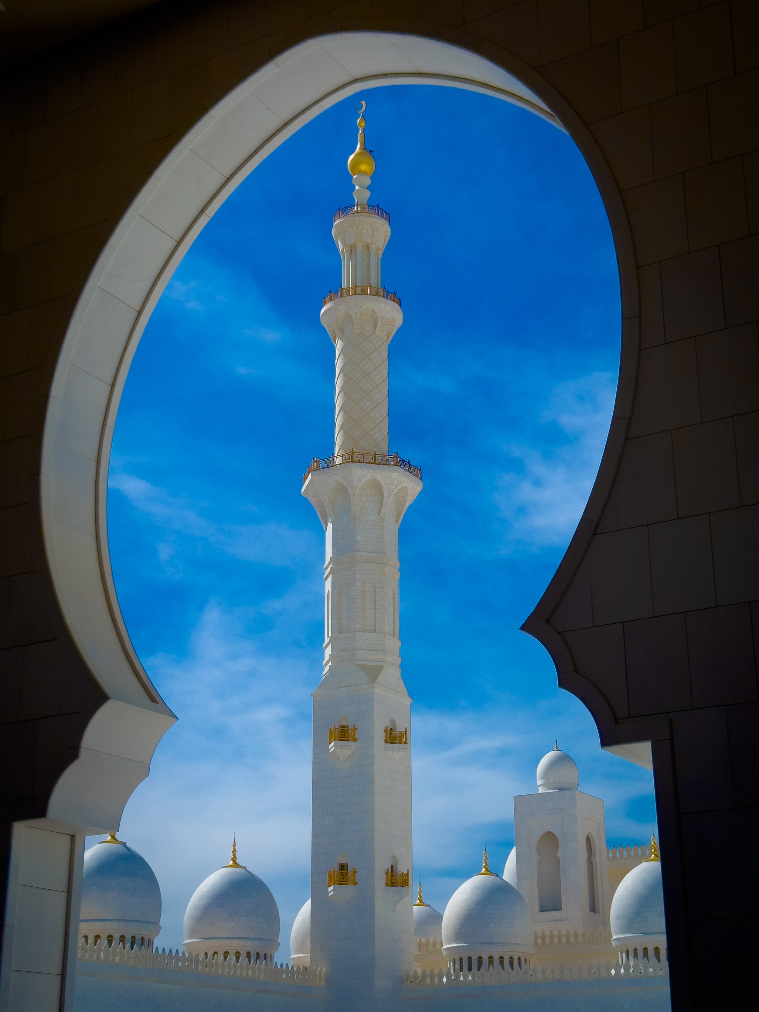 White mosque minaret seen through an archway with blue sky in the background