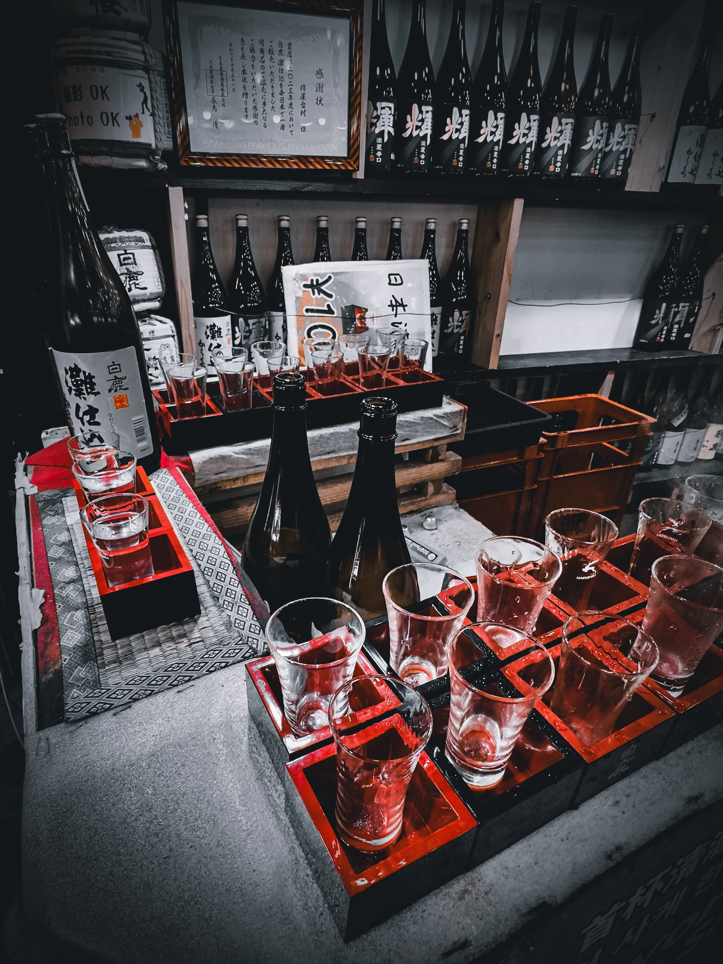 Display of sake bottles, glasses, and related items on a table and shelves in a Japanese bar or restaurant.