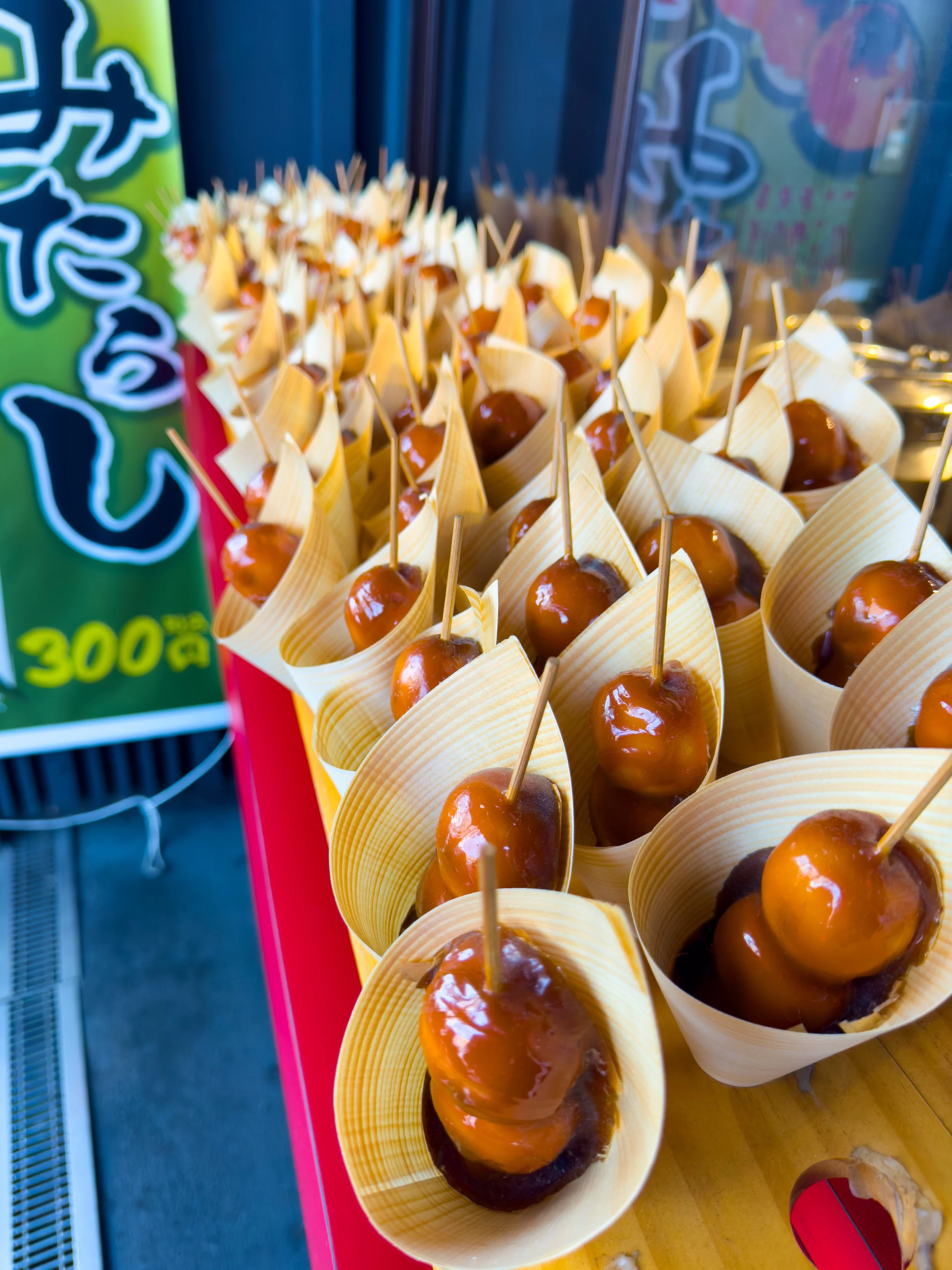 Caramel-coated candied apples on sticks served in small paper cups at a street stall.