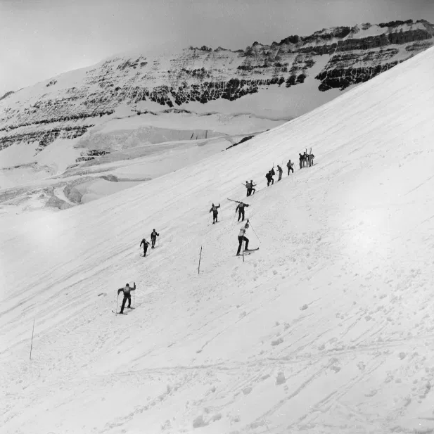   Slalom skiers gather on Victoria Glacier (near Lake Louise) in 1956, for the 6th annual event. “As the race was held on a glacier, there was serious danger of crevasses, so warden Walter Perren ‘went over the area and marked out a safe ski run’.” –