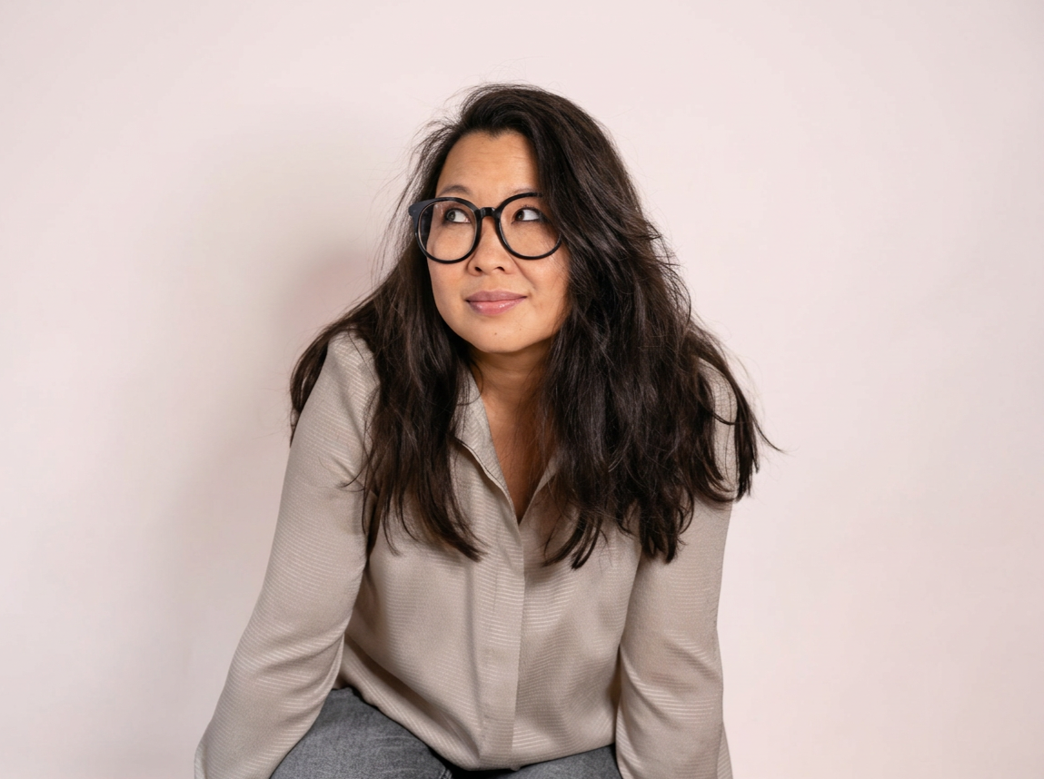 Vrouw met bruin haar en bril die naar links kijkt, zittend tegen een witte achtergrond.