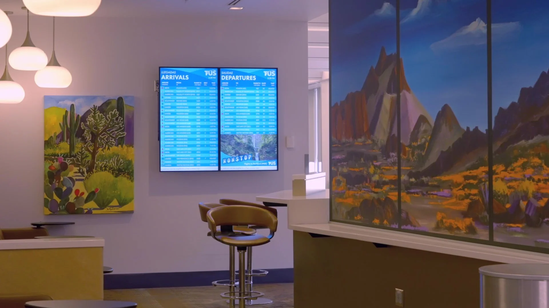 Modern airport terminal interior with flight information displays mounted on wall showing arrivals and departures, with seating area and large landscape mural