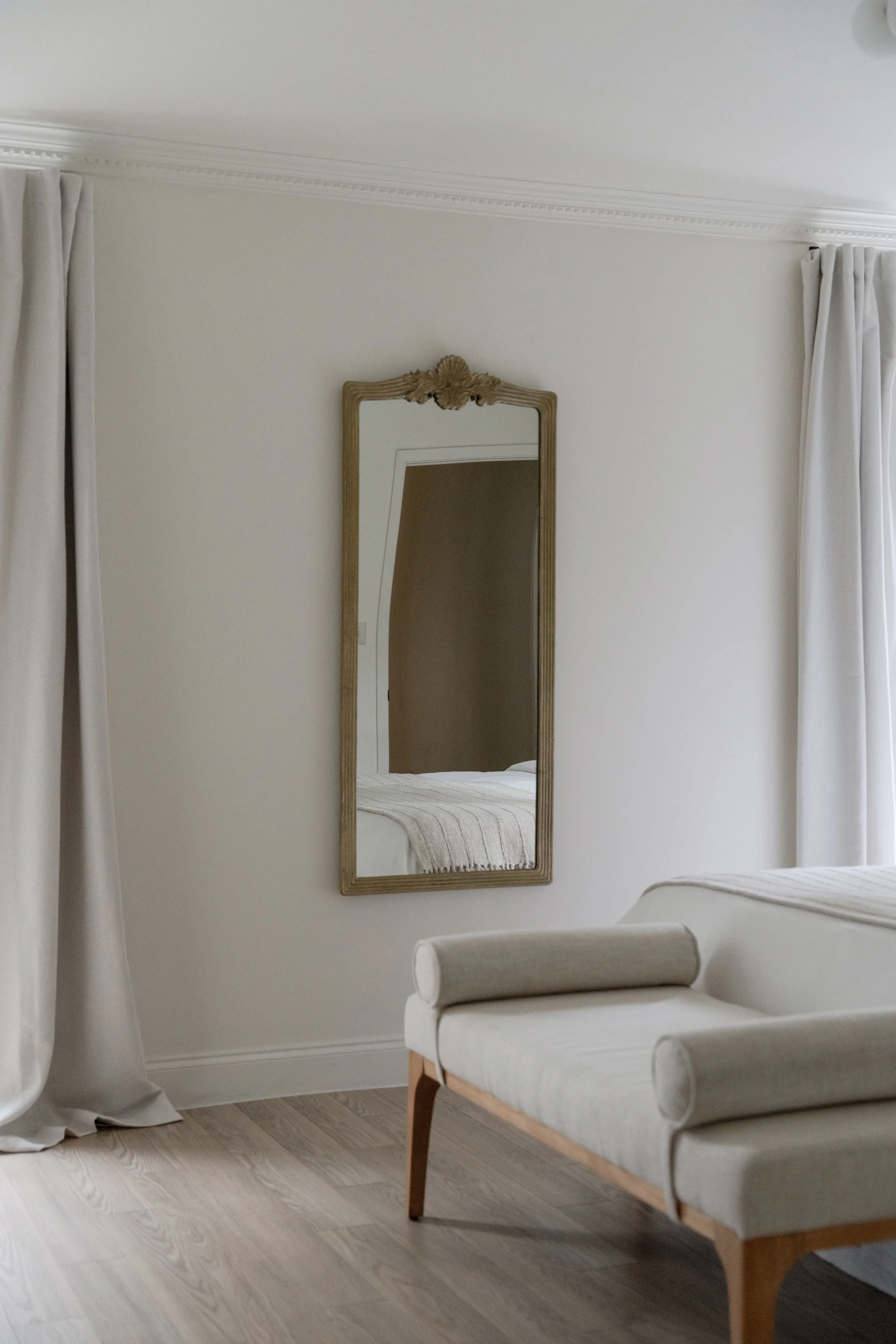 Minimalist bedroom with a large mirror, bench, and soft curtains.