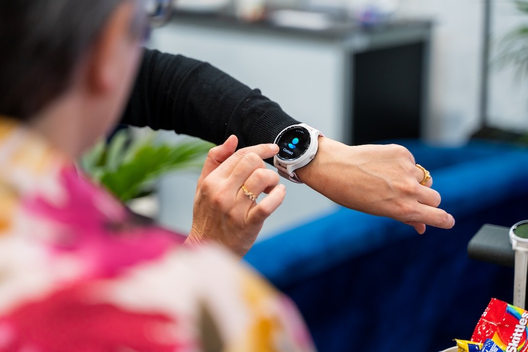 Person wearing a smartwatch with a white band checks the time, with colorful clothing and snacks visible in the background.
