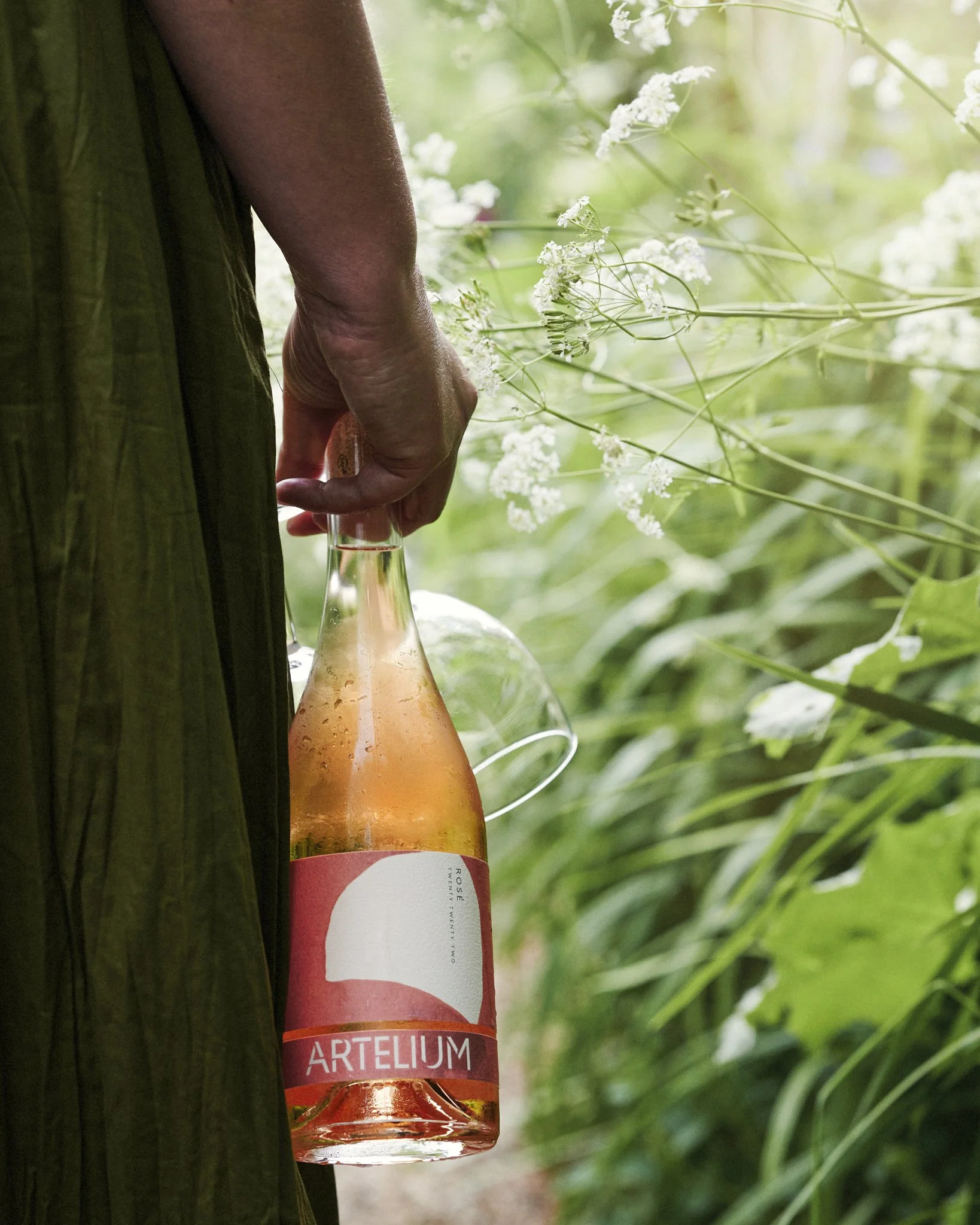 Artelium Rosé 2023 bottle and glass held by woman in green dress in leafy undergrowth 