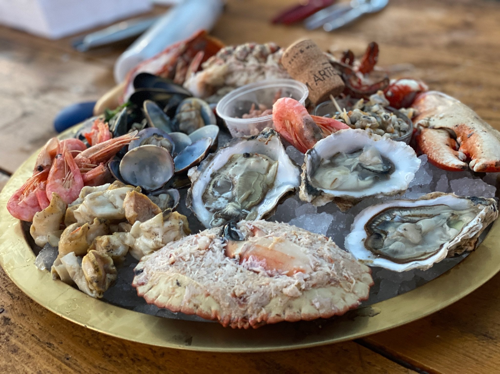 Seafood platter with oysters, shrimp, mussels, lobster, and crab on crushed ice, served on a gold-colored tray.