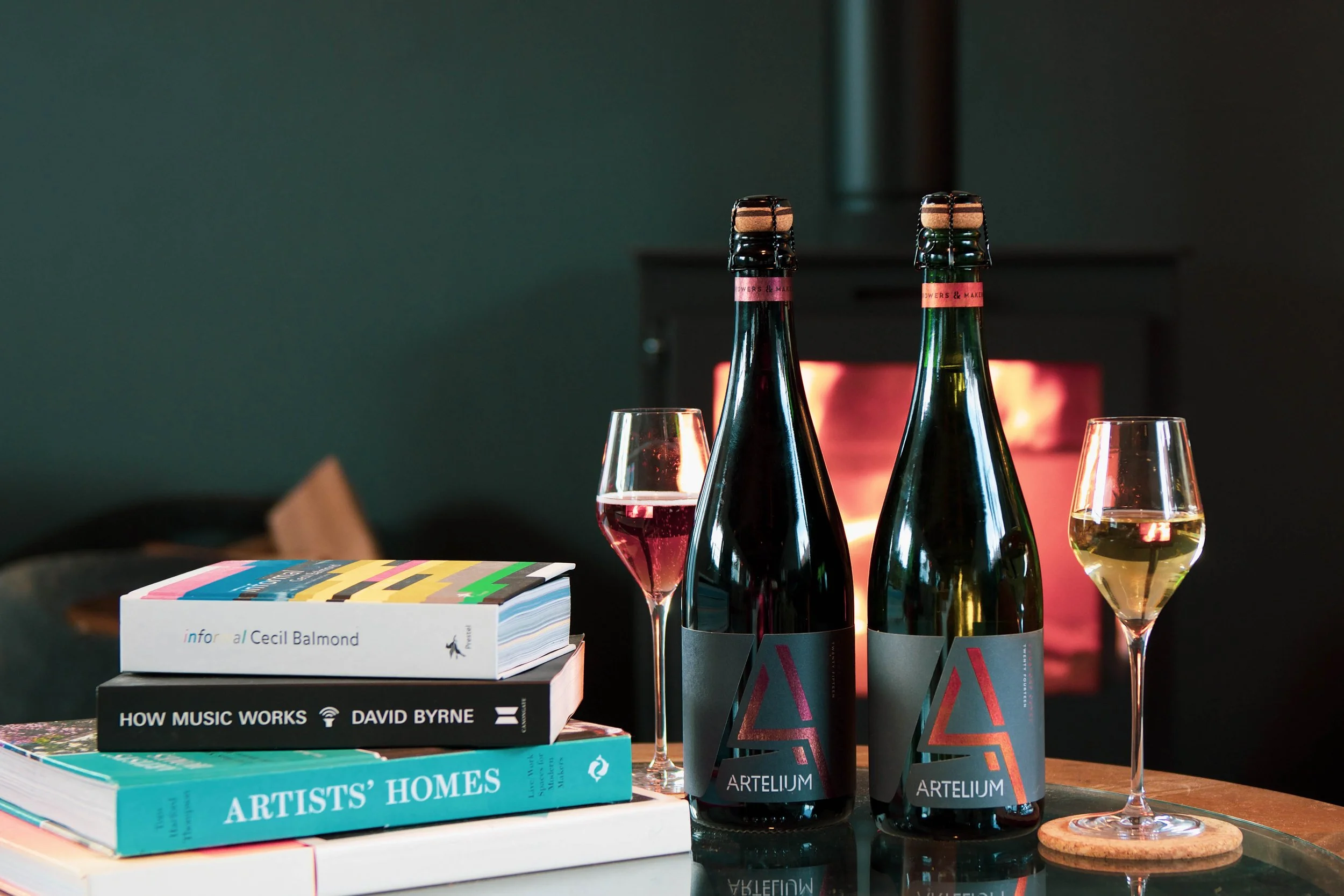 Artelium Curators Cuvée and Makers Rosé in front of fire with book stack 