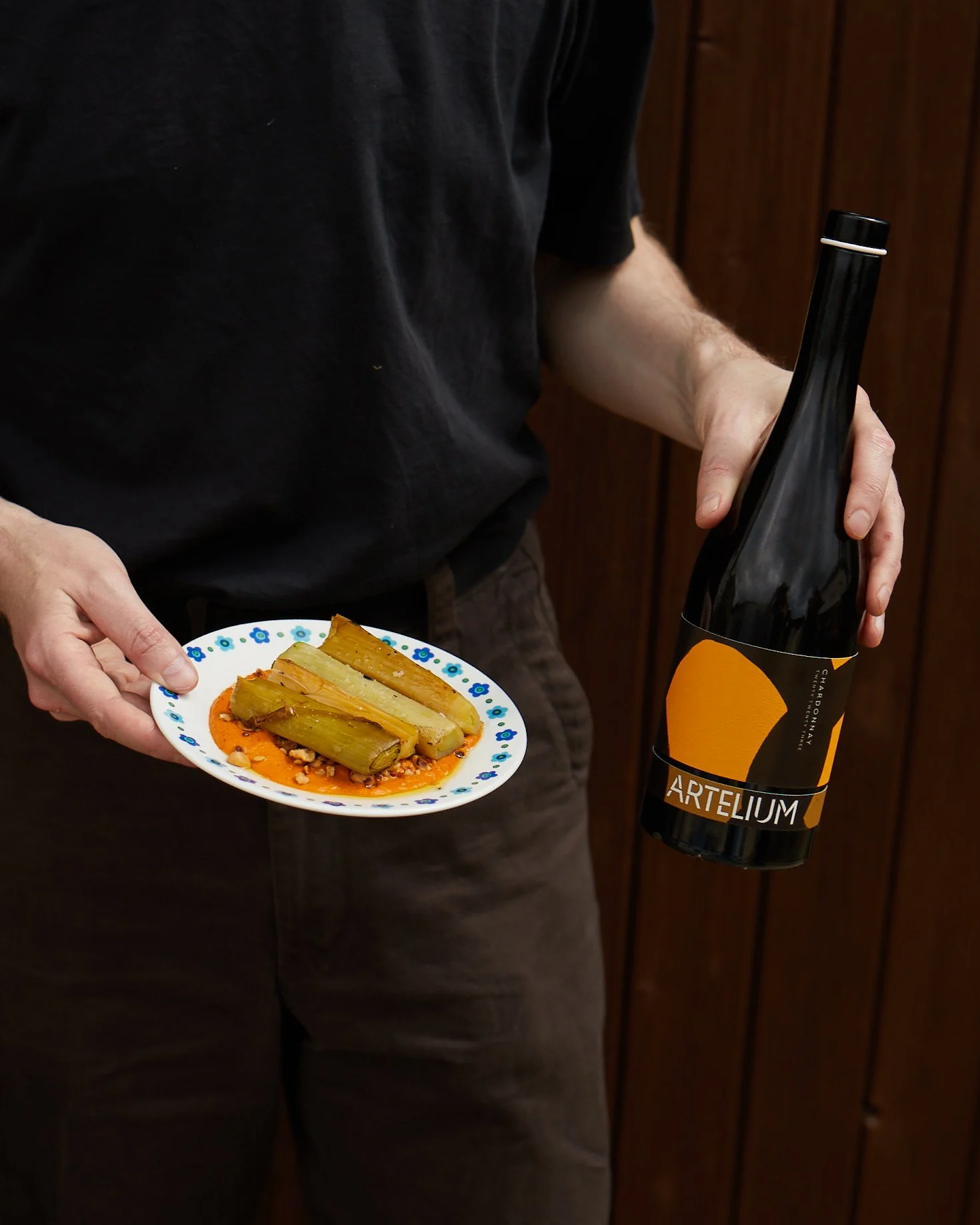 Artelium Chardonnay 2023 with dish of grilled leeks in front of dark background 