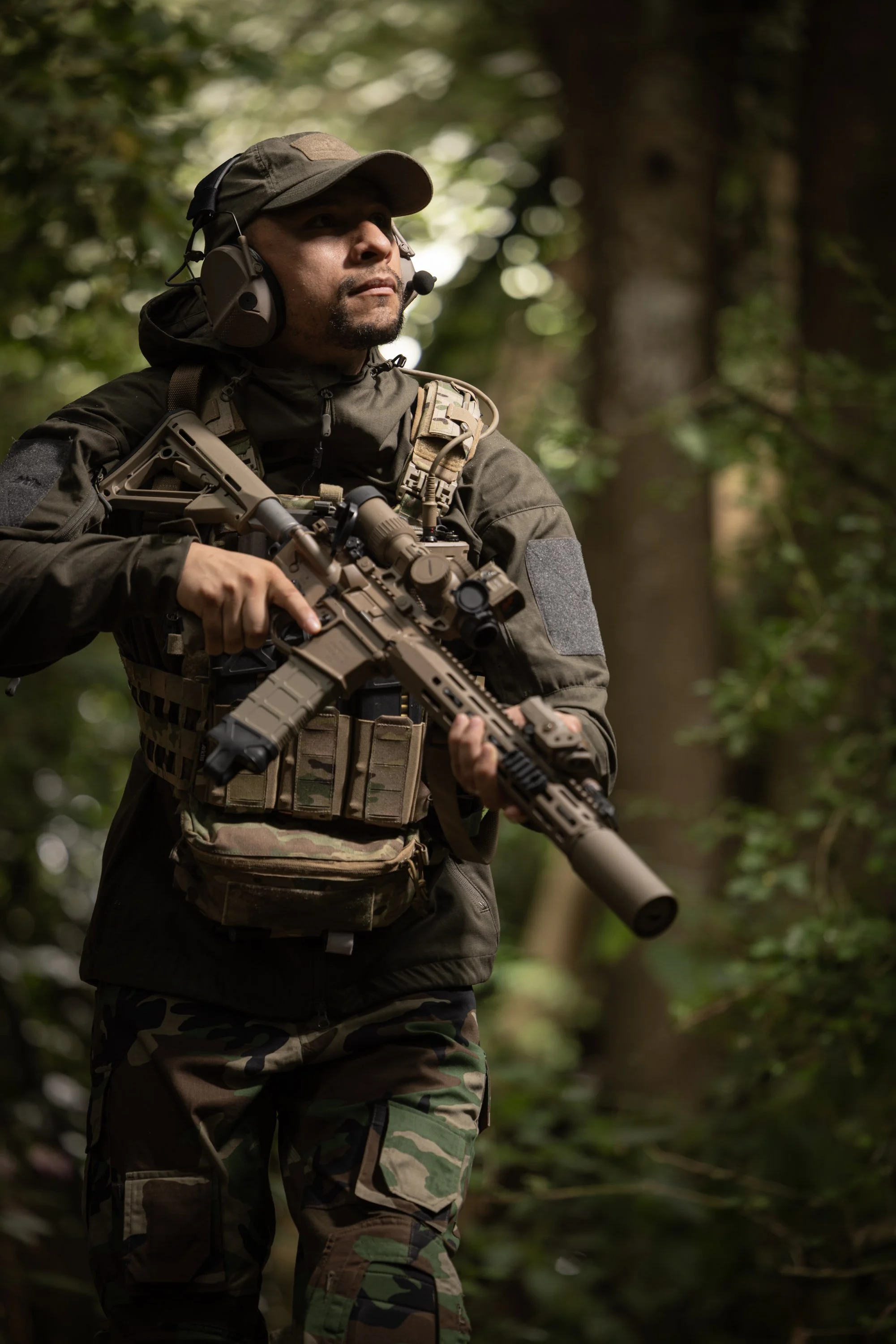 A soldier dressed in camouflage uniform and tactical gear holding a rifle in a forest.