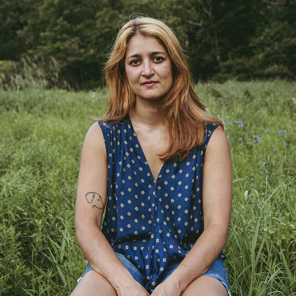 Erica is wearing a polka dotted blue shirt sitting in a field