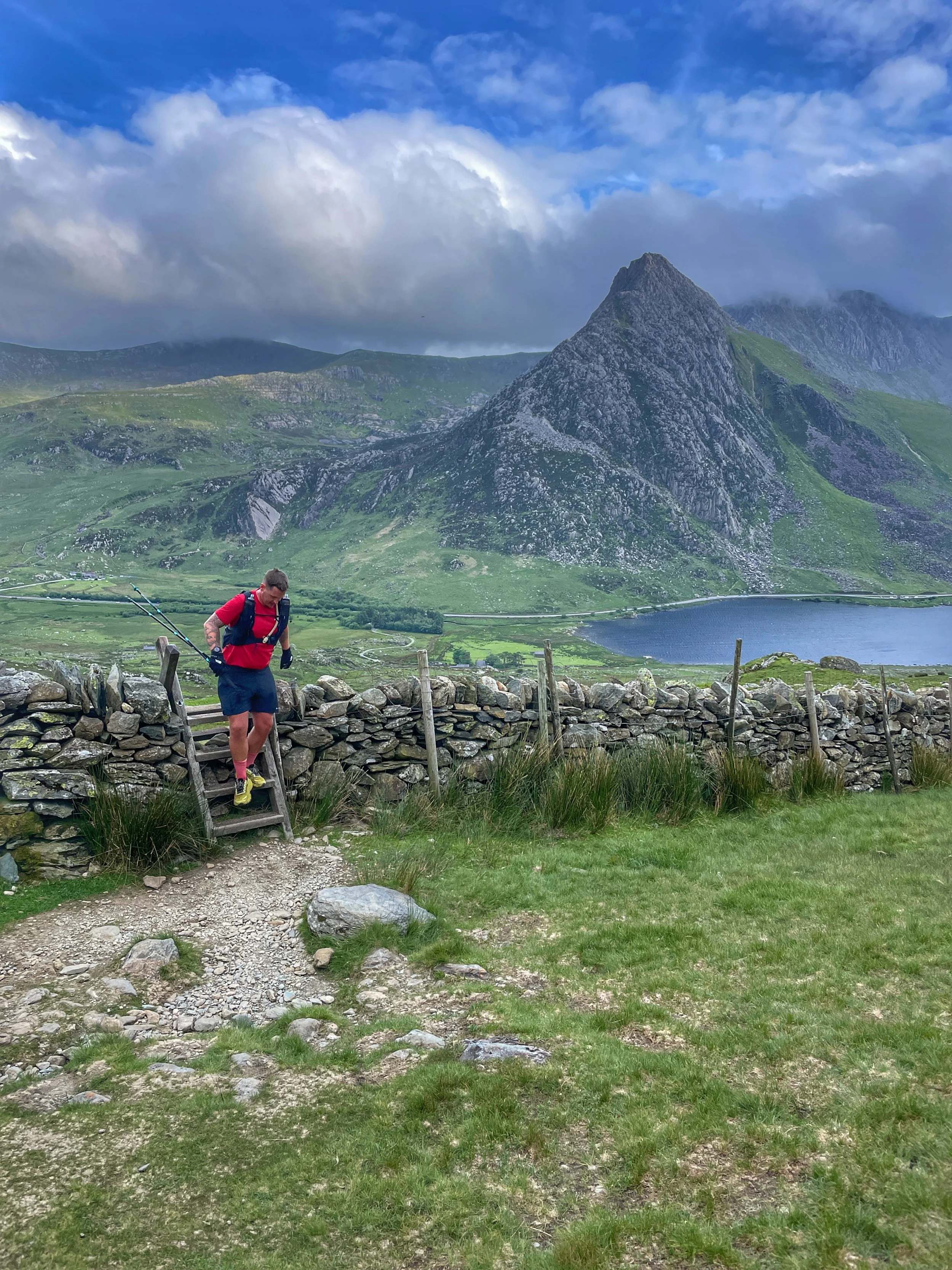Hiker crossing a stile on his way to climb Pen Yr Ole wen with Tryfan in the background in Snowdonia national park.