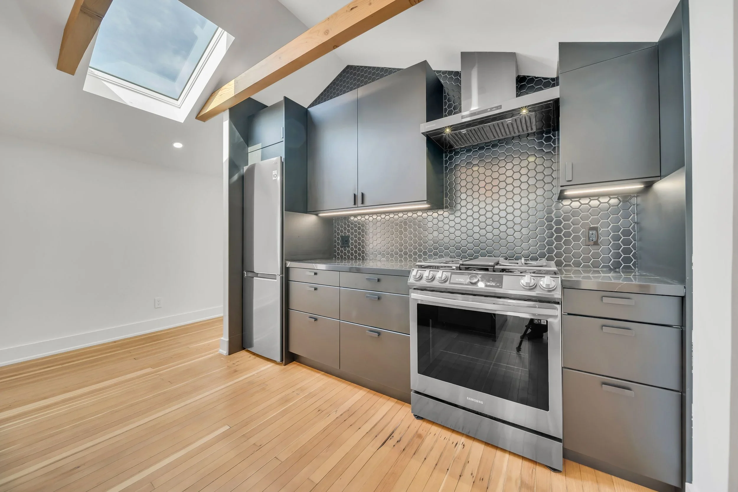 Modern kitchen with hexagonal backsplash, skylight, and black cabinets in Guelph by Odin Agnuk