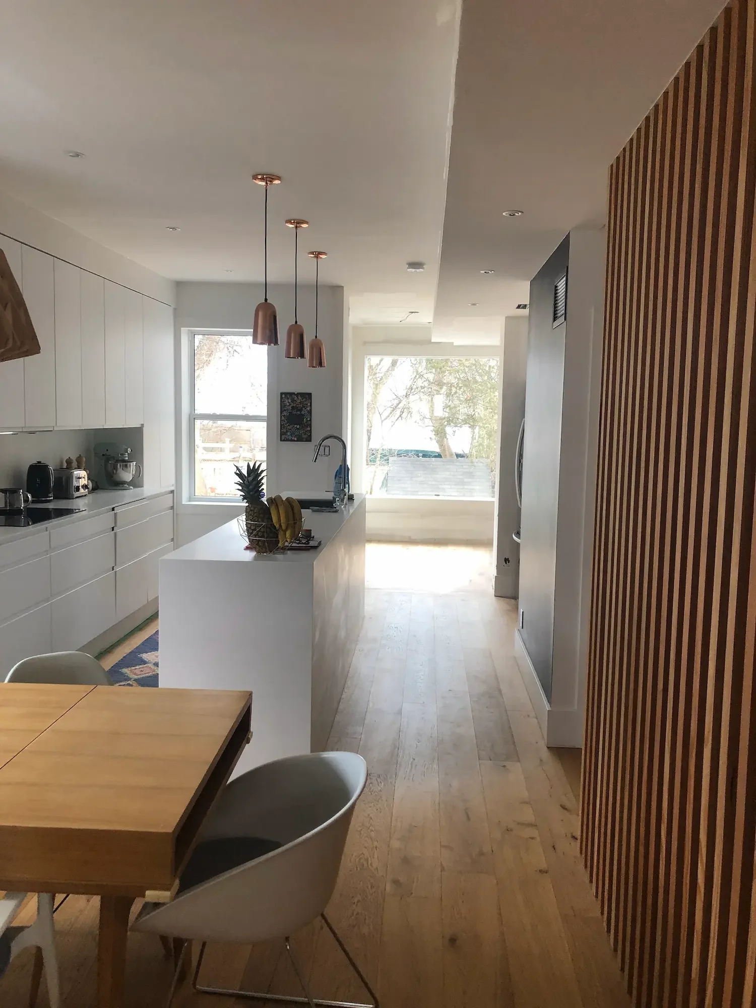 Modern kitchen renovation with copper pendant lights, white countertops, and hardwood floors by Odin Agnuk