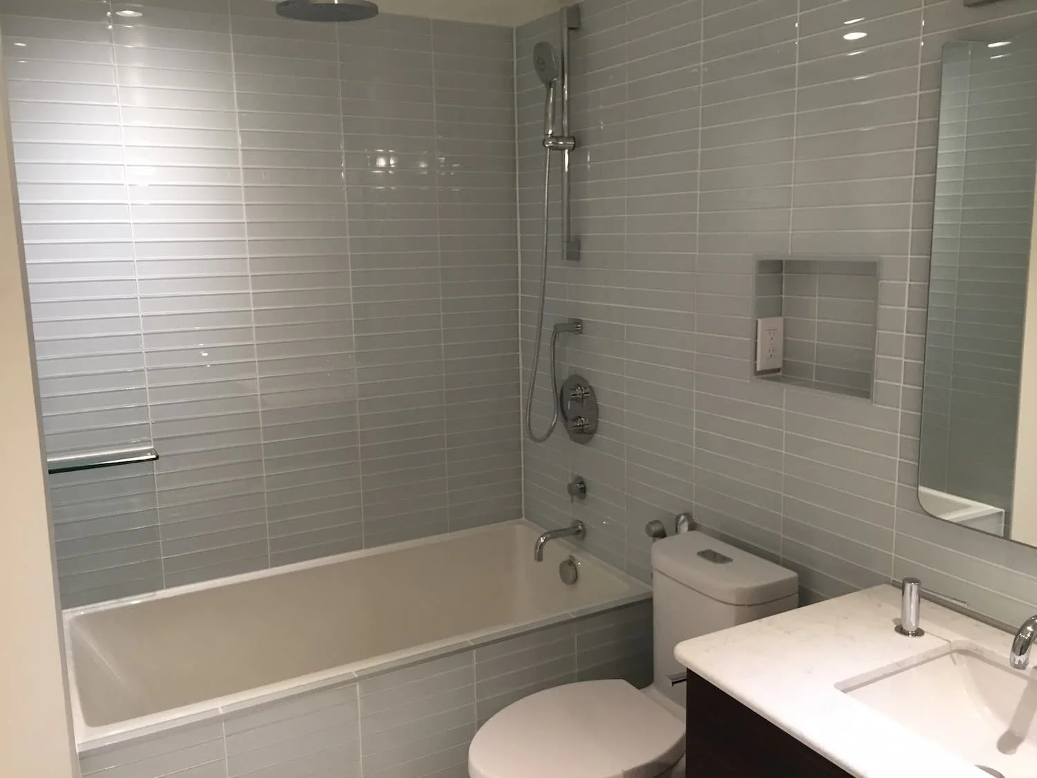 Bathroom renovation with glass subway tile and tub shower combo with rain head - Grey County by Odin Agnuk