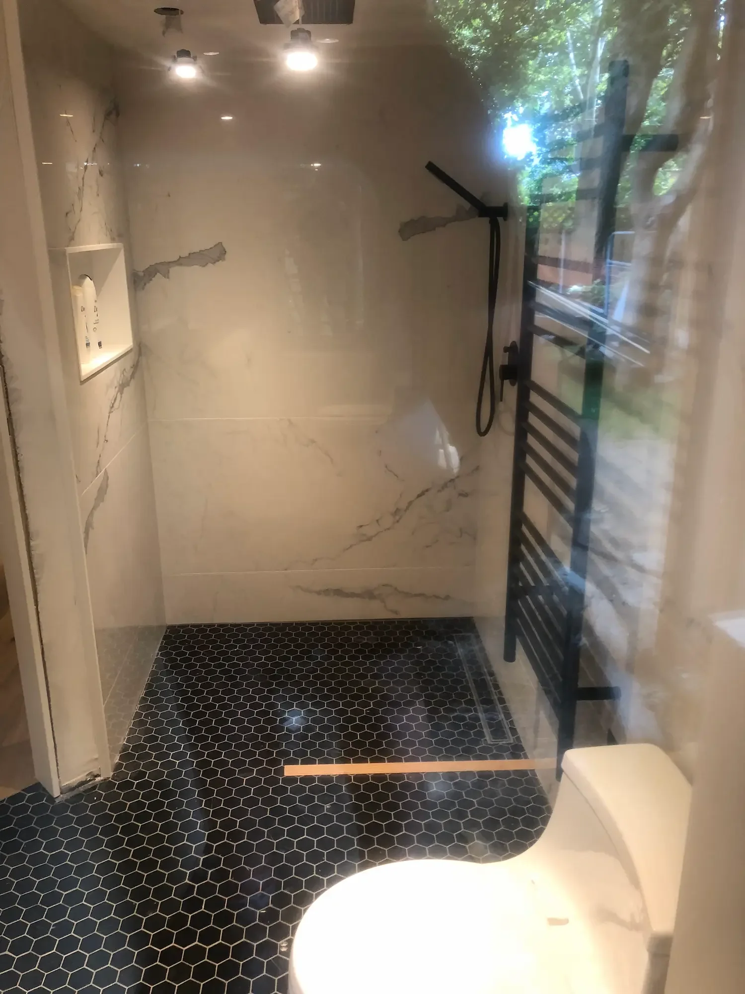 Walk-in shower with ceiling rain head, glass panel, and black heated towel rack - The Beaches by Odin Agnuk
