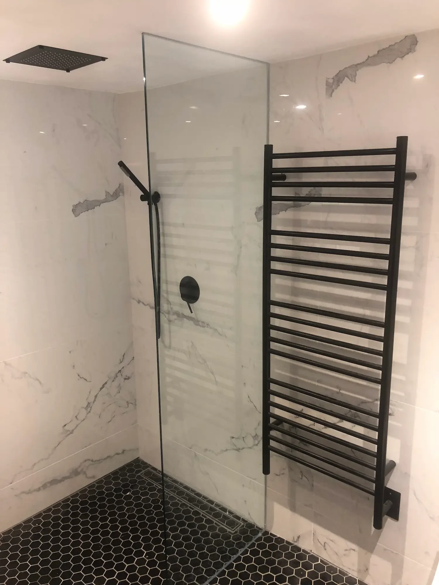 Walk-in shower with marble walls, black hexagon floor tile, and heated towel rack - The Beaches Toronto by Odin Agnuk