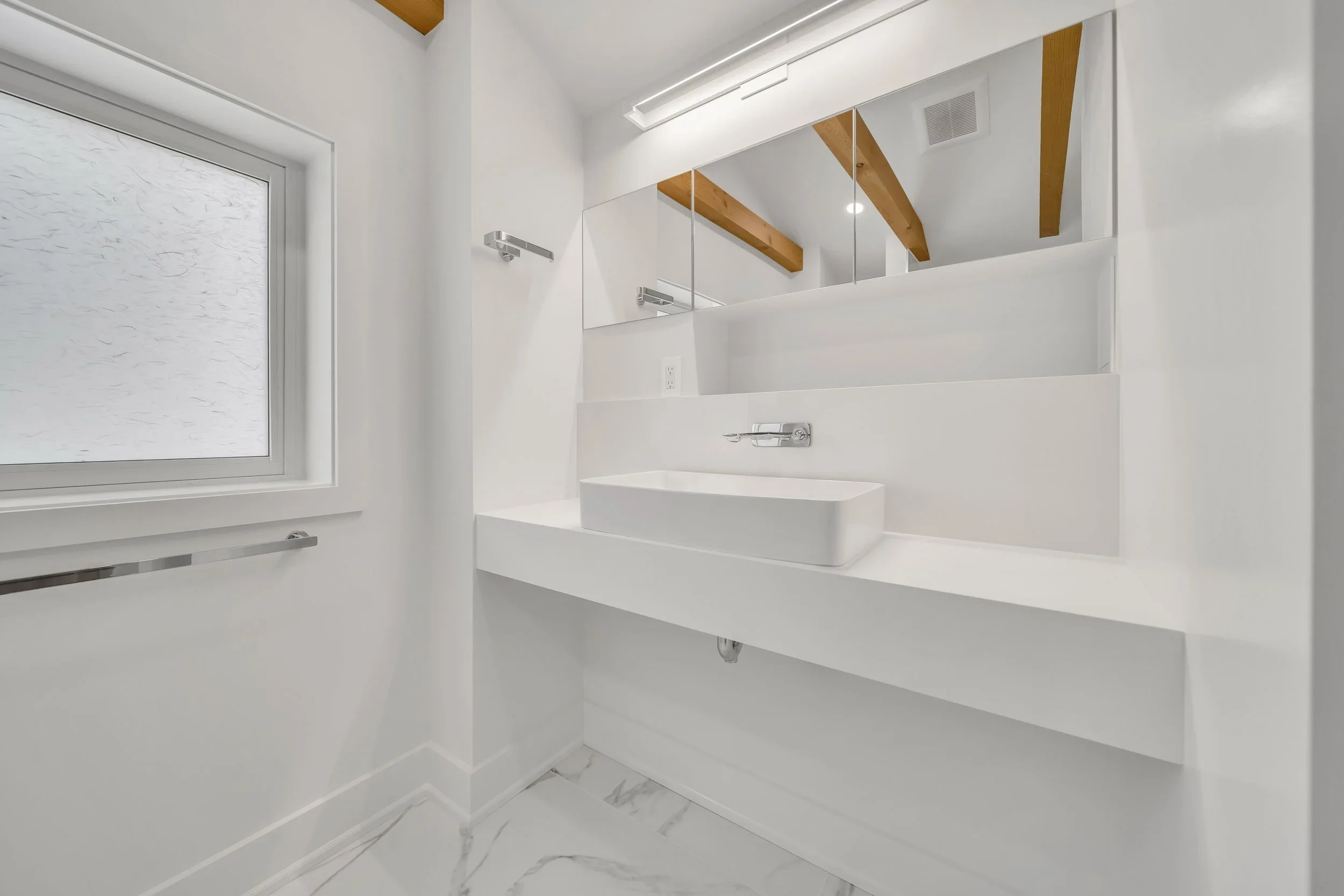 White bathroom with floating vanity, vessel sink, and exposed wood beams in Guelph century home renovation by Odin Agnuk