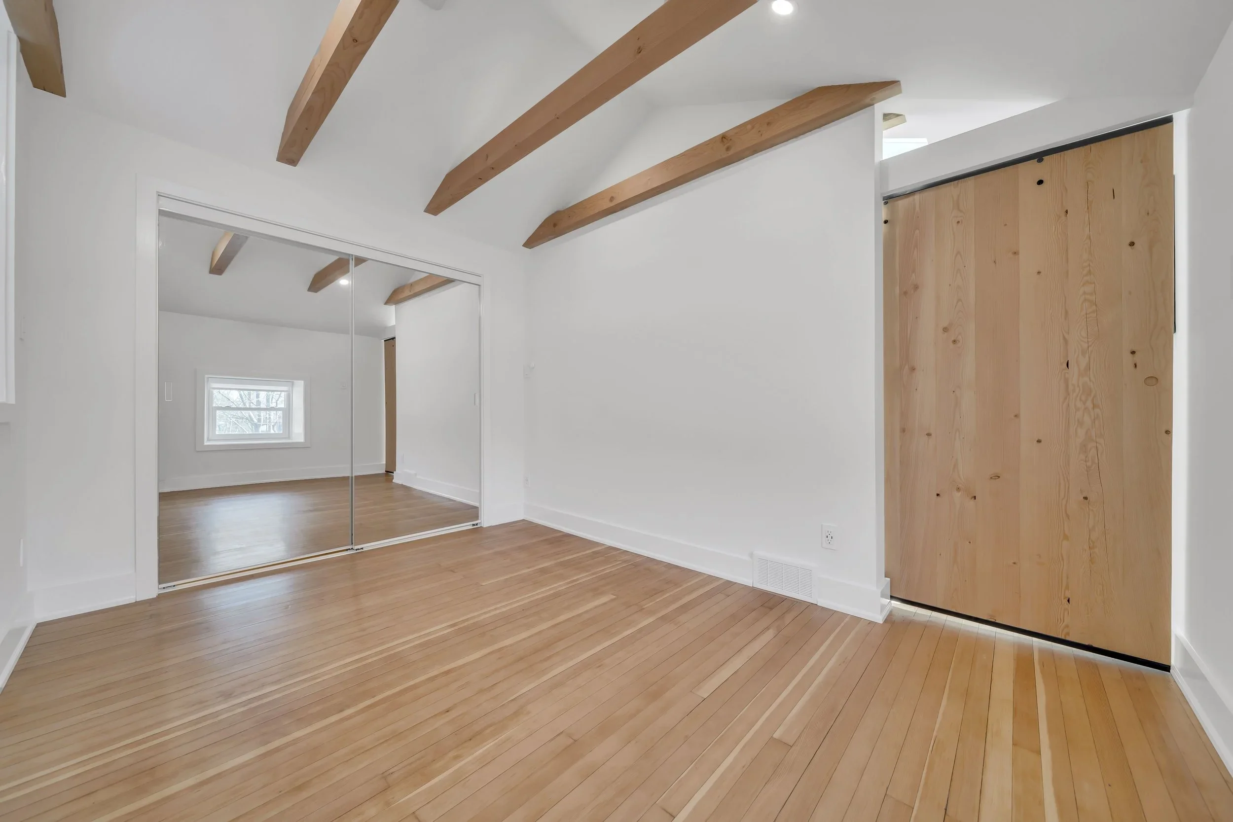 Bedroom with mirrored closet doors, fir barn door, and exposed wood beams in Guelph renovation by ODIN+AGNUK