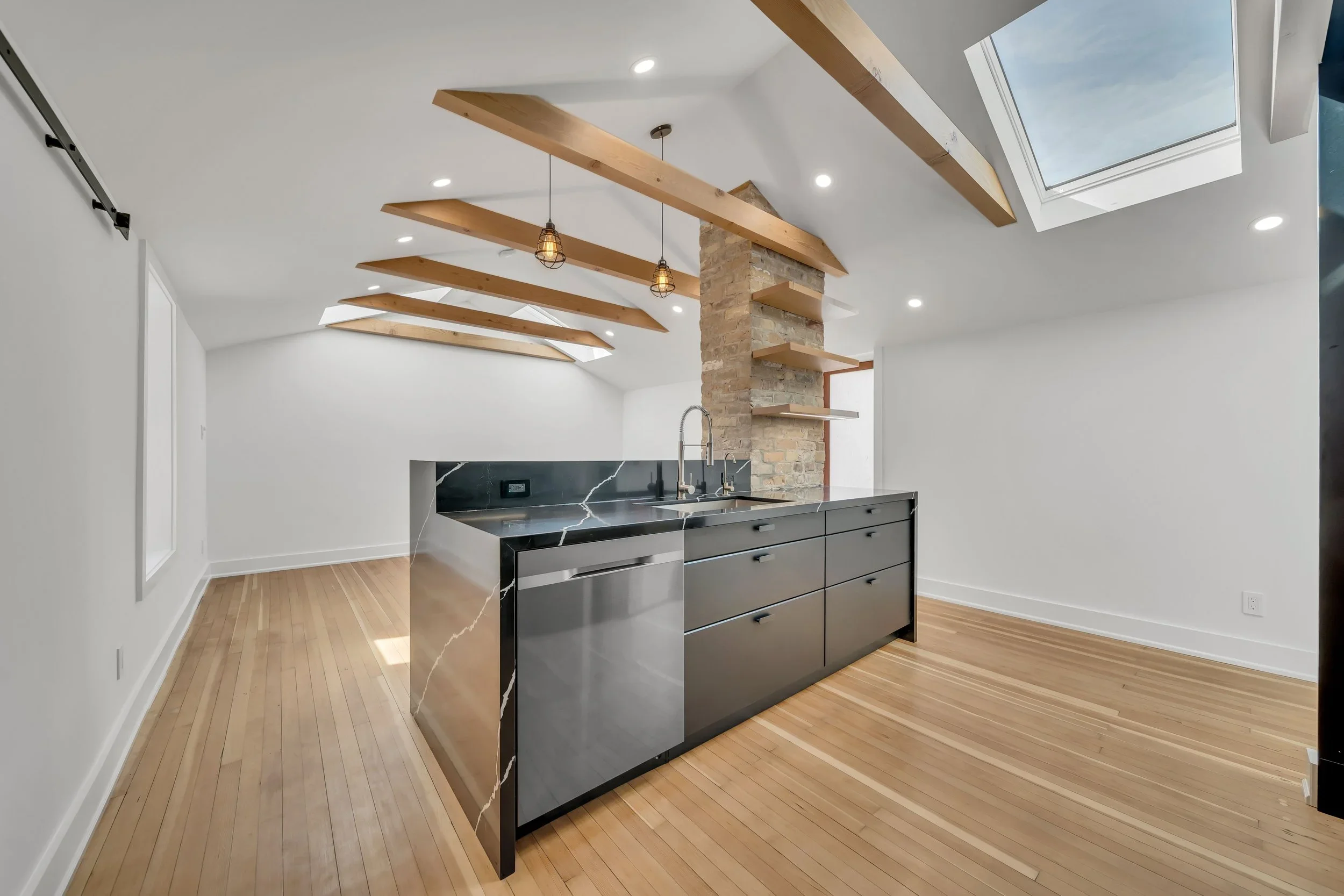 Kitchen island with waterfall counter, skylights, and exposed brick column in Guelph by ODIN+AGNUK