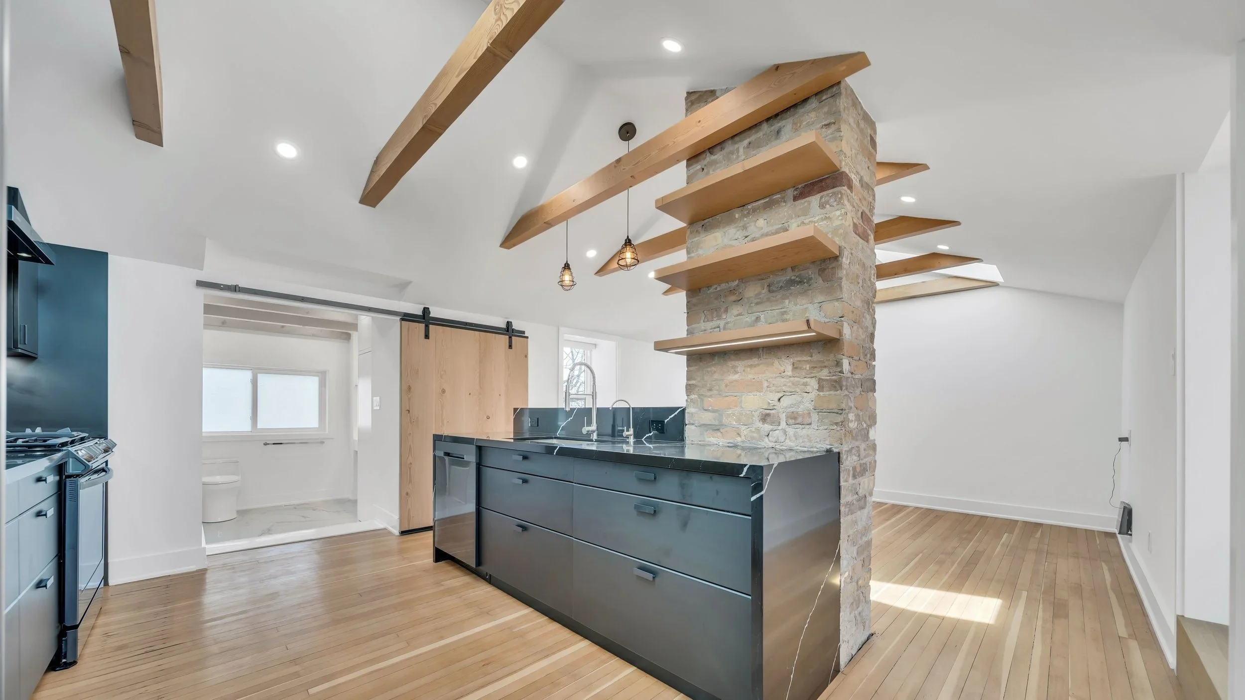 Open concept kitchen with exposed brick, wood beams, waterfall island, and barn door in Guelph by Odin Agnuk