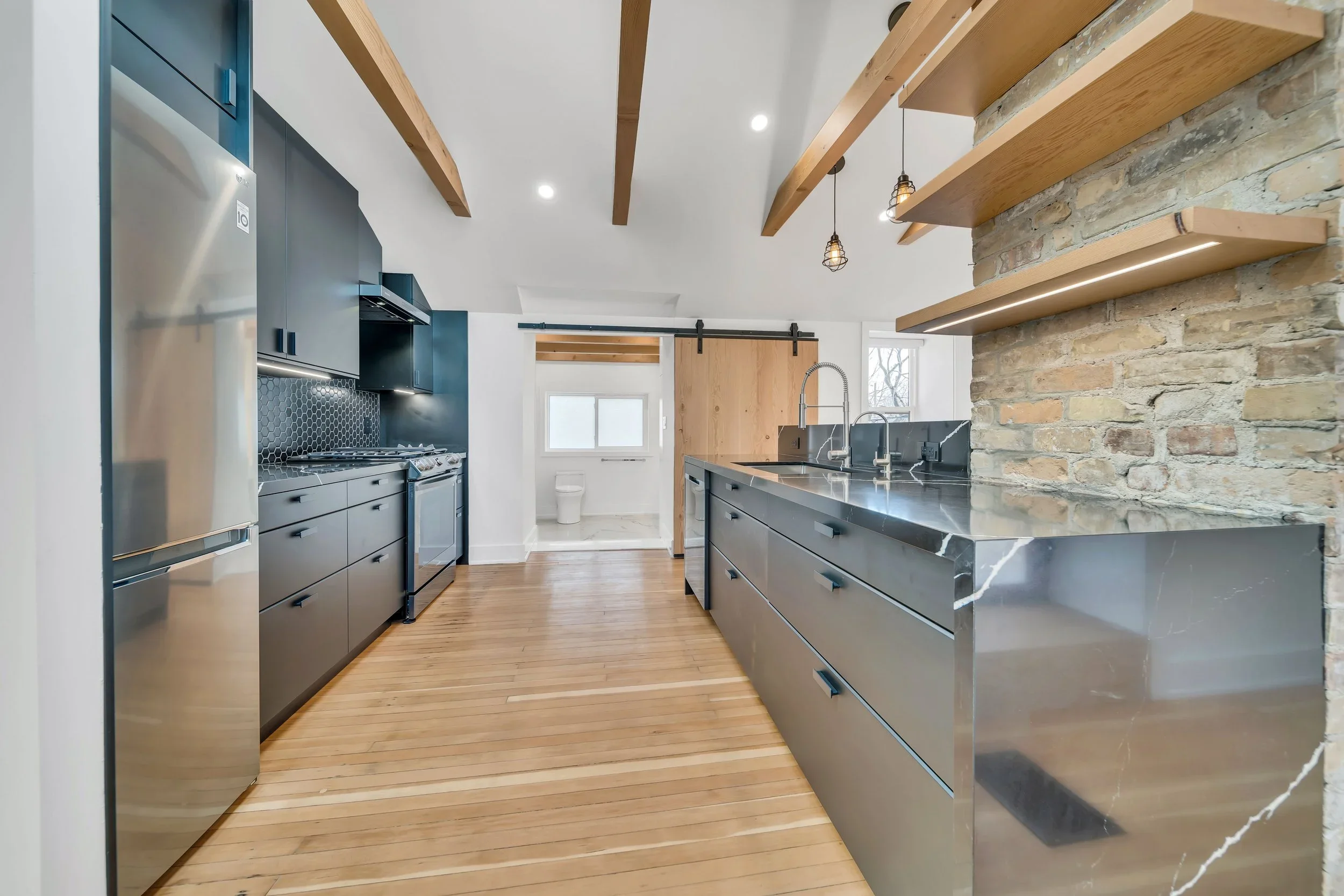 Kitchen with exposed brick, wood beams, floating shelves with LED lighting, and waterfall countertop in Guelph by ODIN+AGNUK.