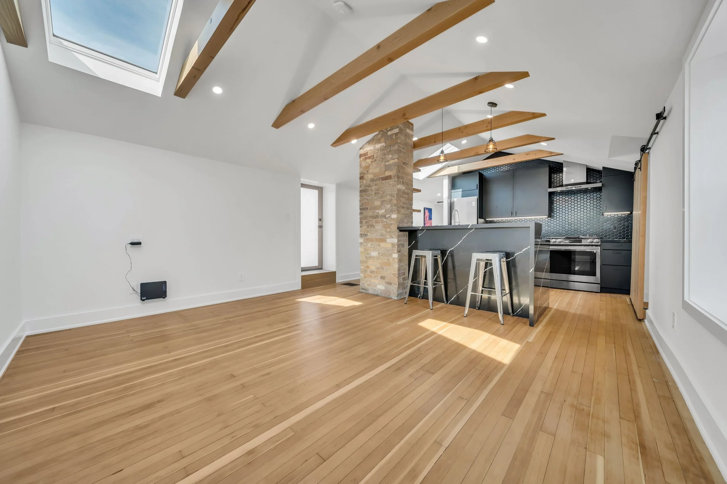 Open concept living space with skylights, wood beams, and modern kitchen in Guelph century home by ODIN+AGNUK