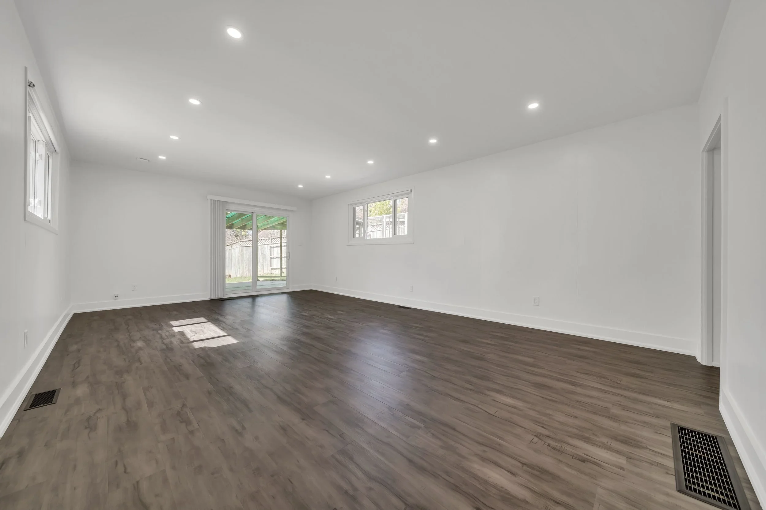 Living room with dark LVP flooring and sliding patio door in Guelph duplex conversion by ODIN+AGNUK