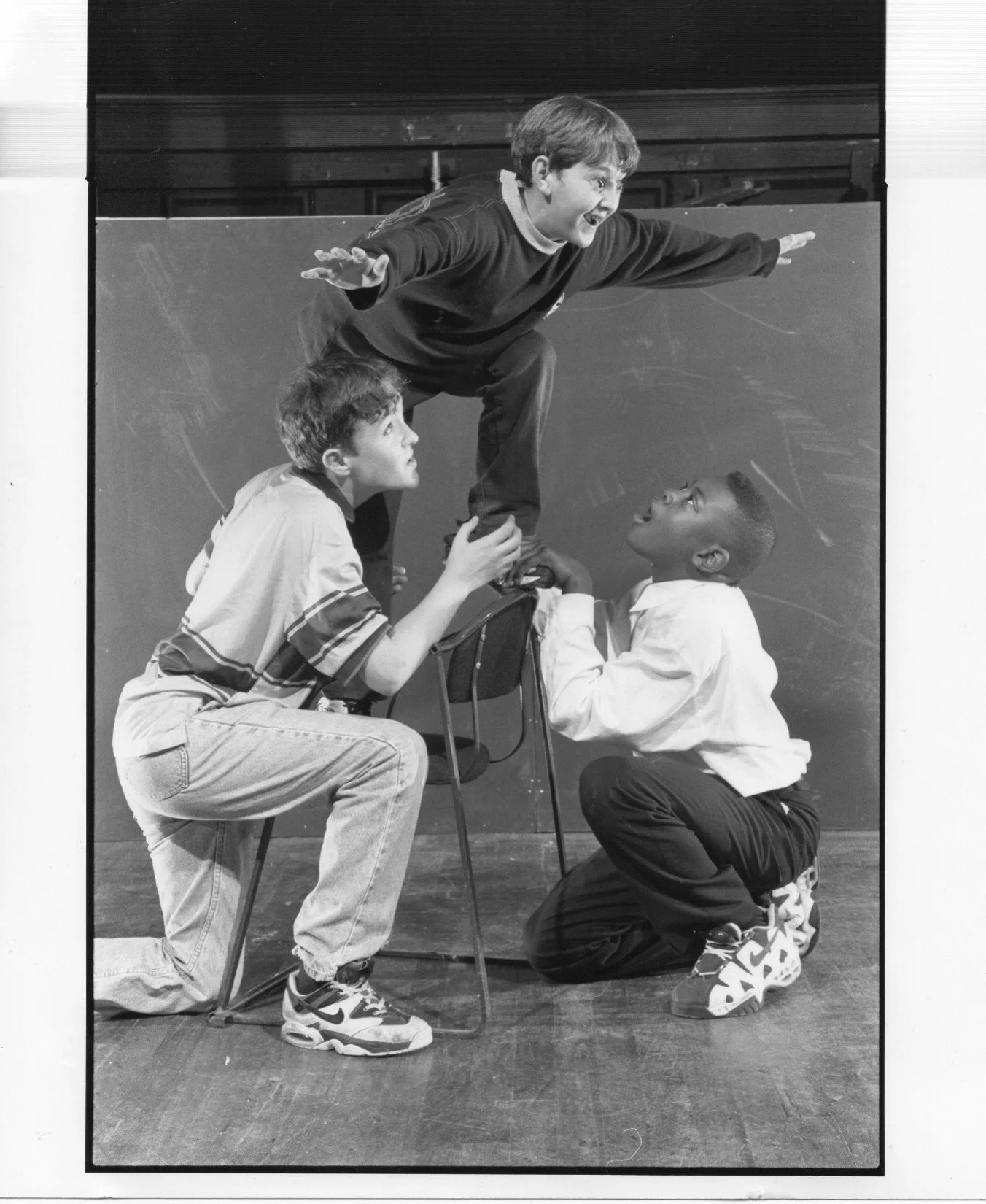 Three young boys, with one elevated on a chair, each with unique facial expressions.