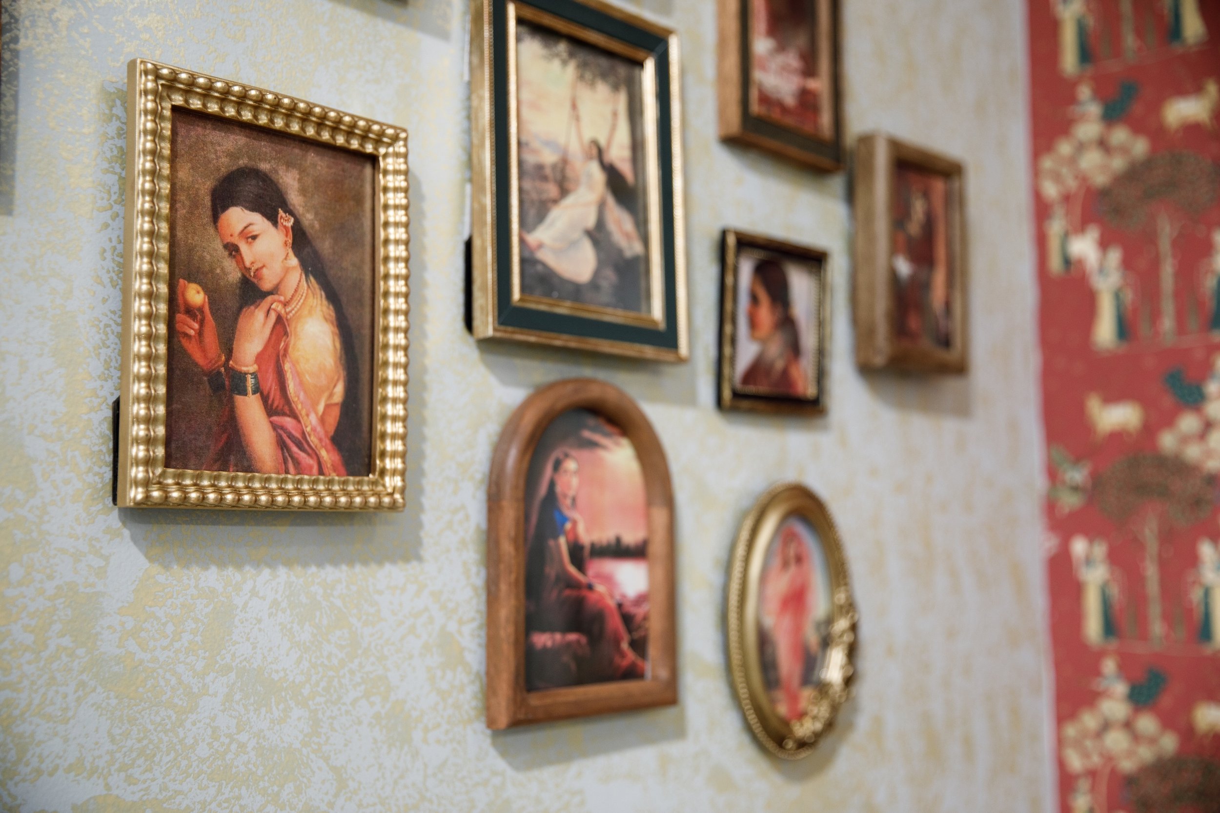 A wall decorated with multiple framed paintings, including portraits of women and one of a woman sitting by a body of water.