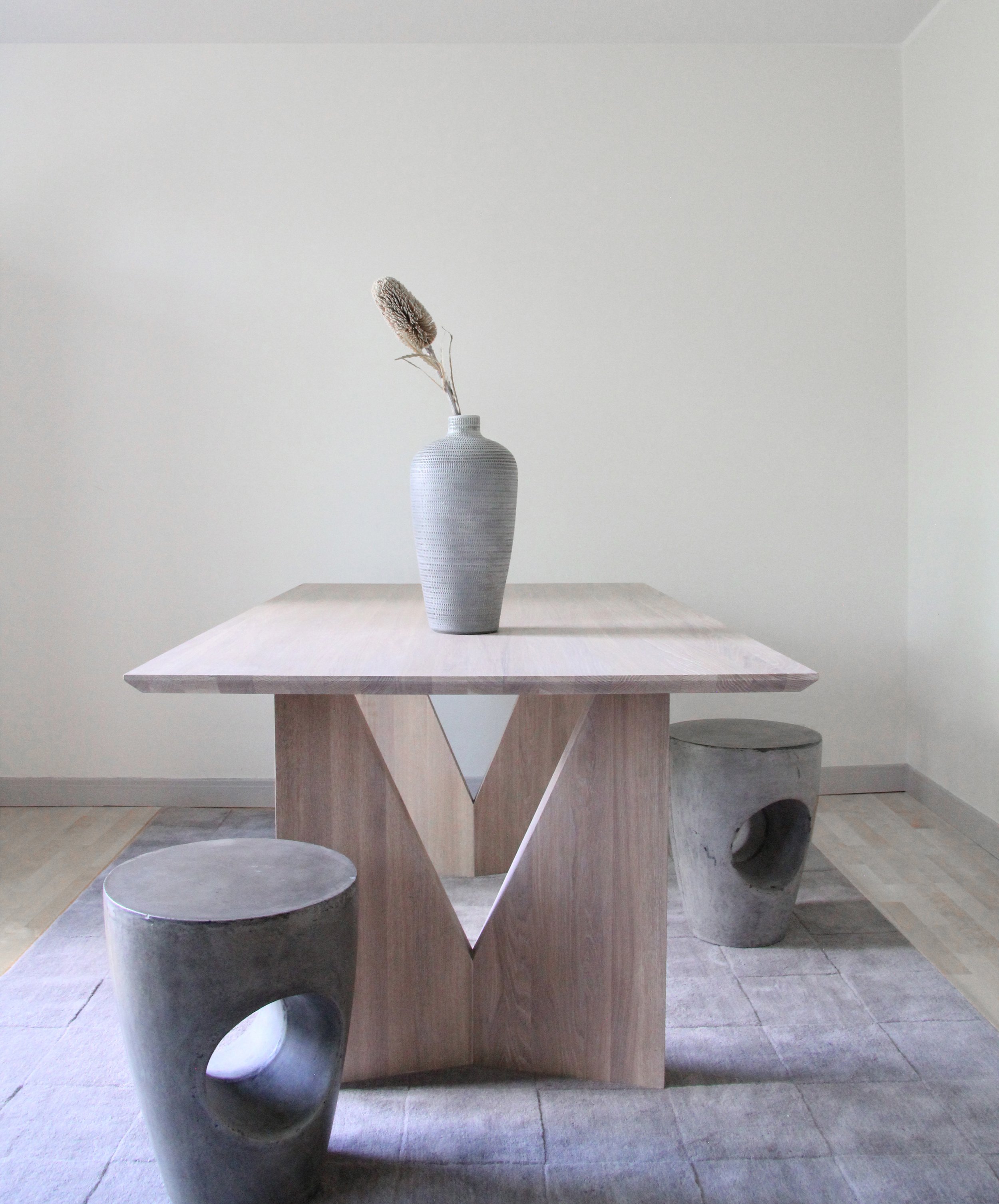 Minimalist room with wooden table, gray vase with dried plant, and unique stools.