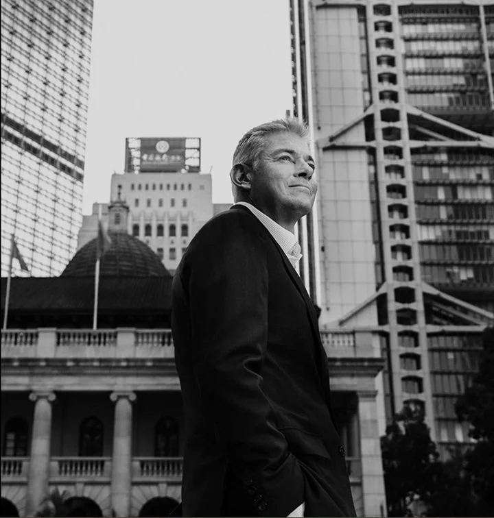 Kevin Bowers looking into the distance and smiling in front of Hong Kong courthouse