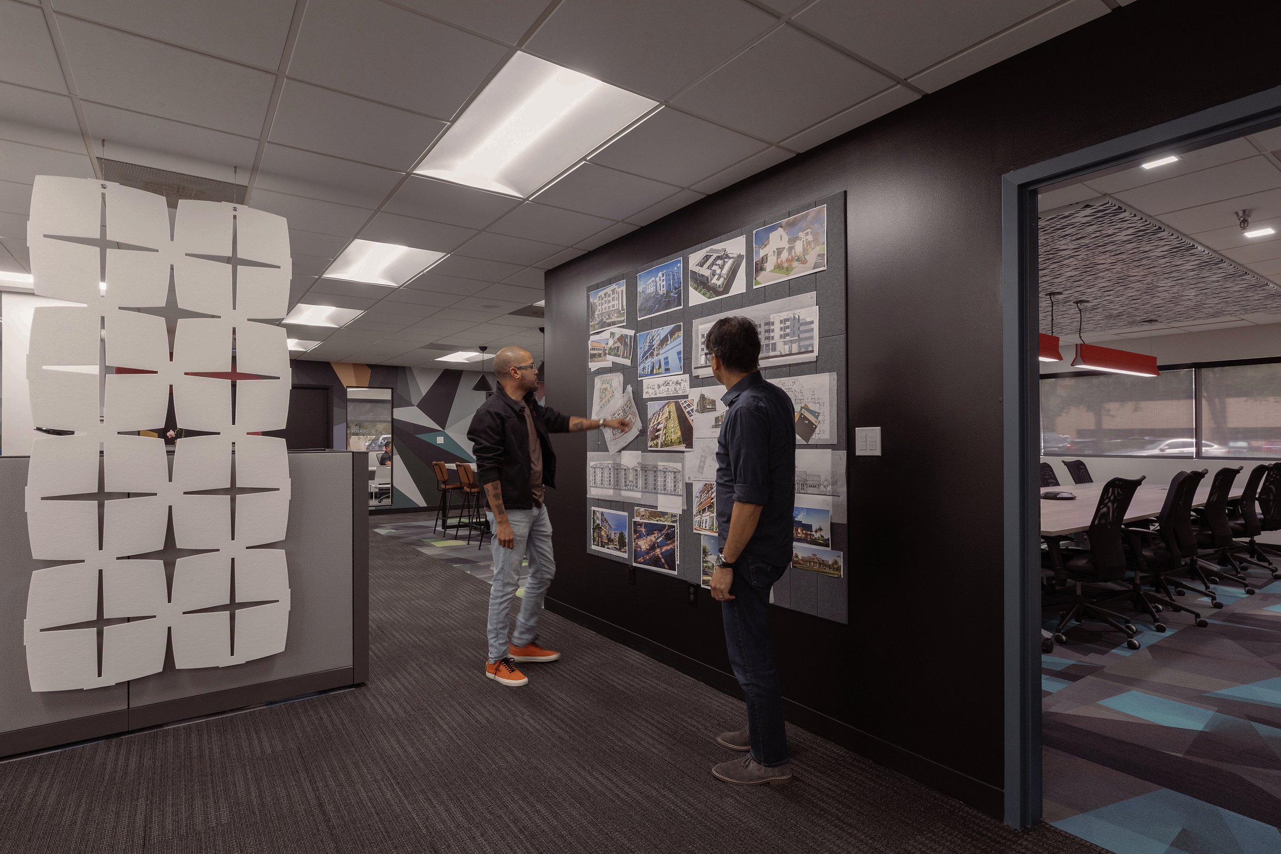 Two men discussing architectural plans and images on a board in a modern office.