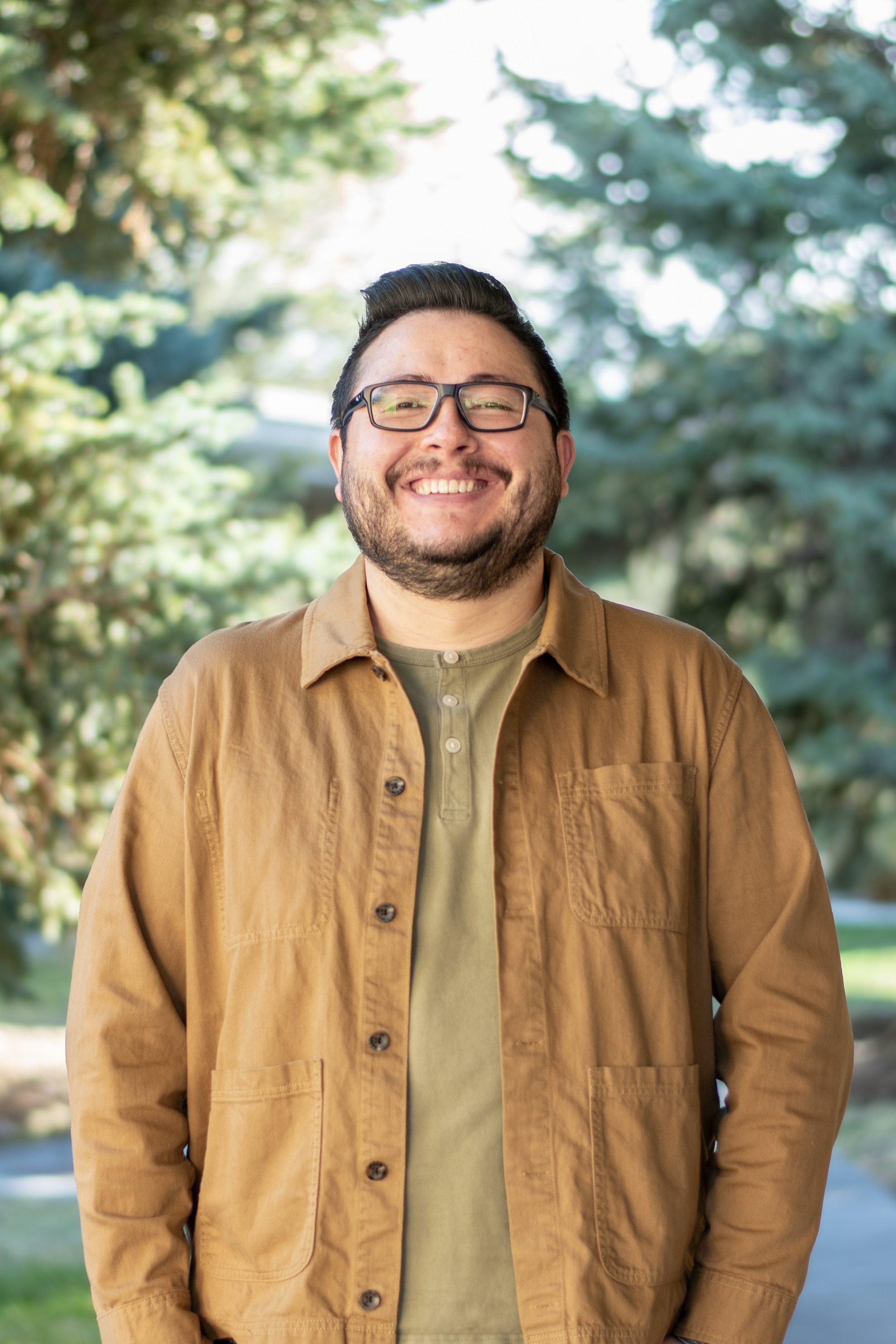 Person with short dark hair and glasses smiles on a sunny day.