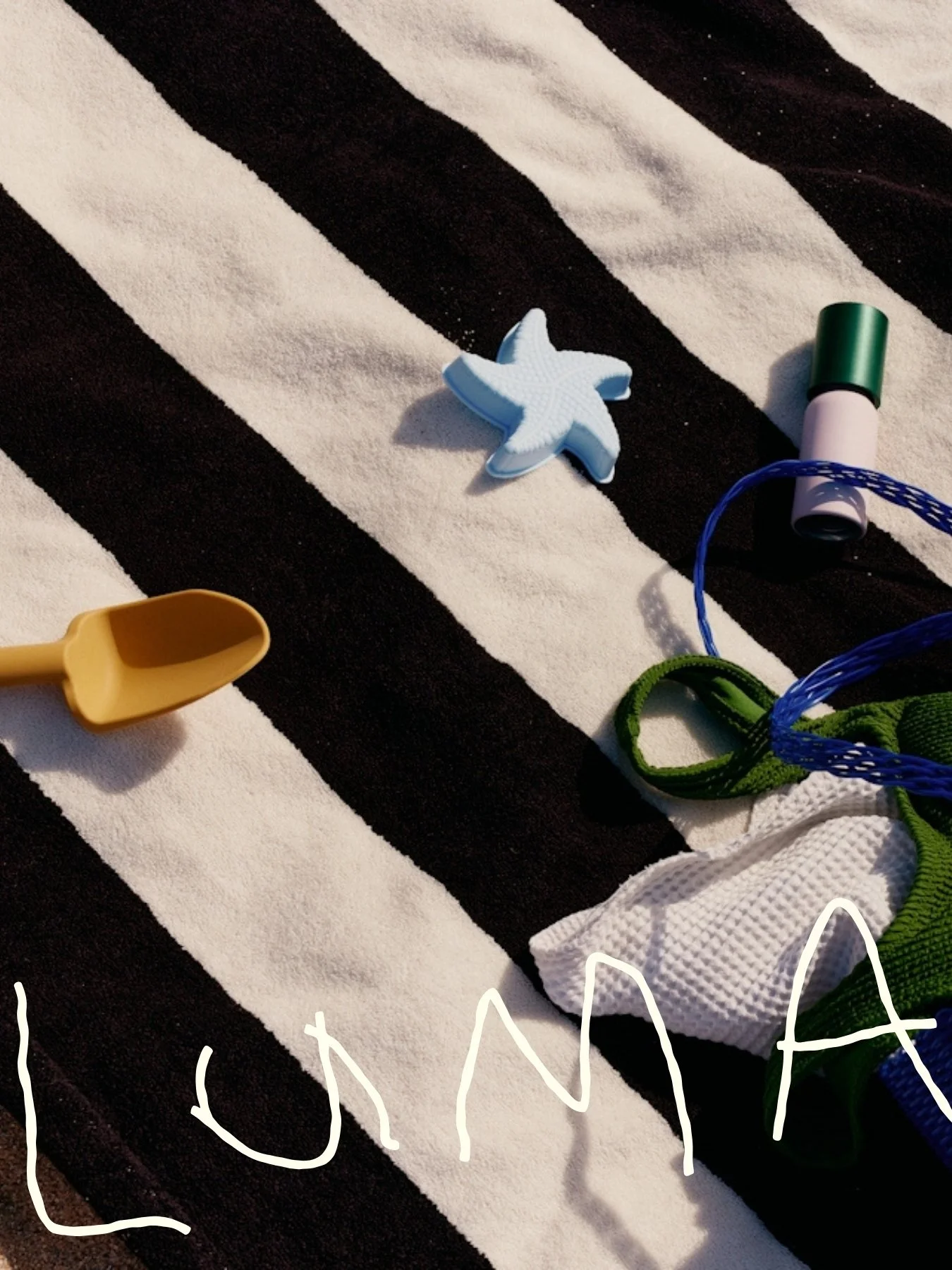 Luma brand lifestyle flat lay of kids beach toys and sunscreen on a striped towel — sun safety brand world photography by Anotherside