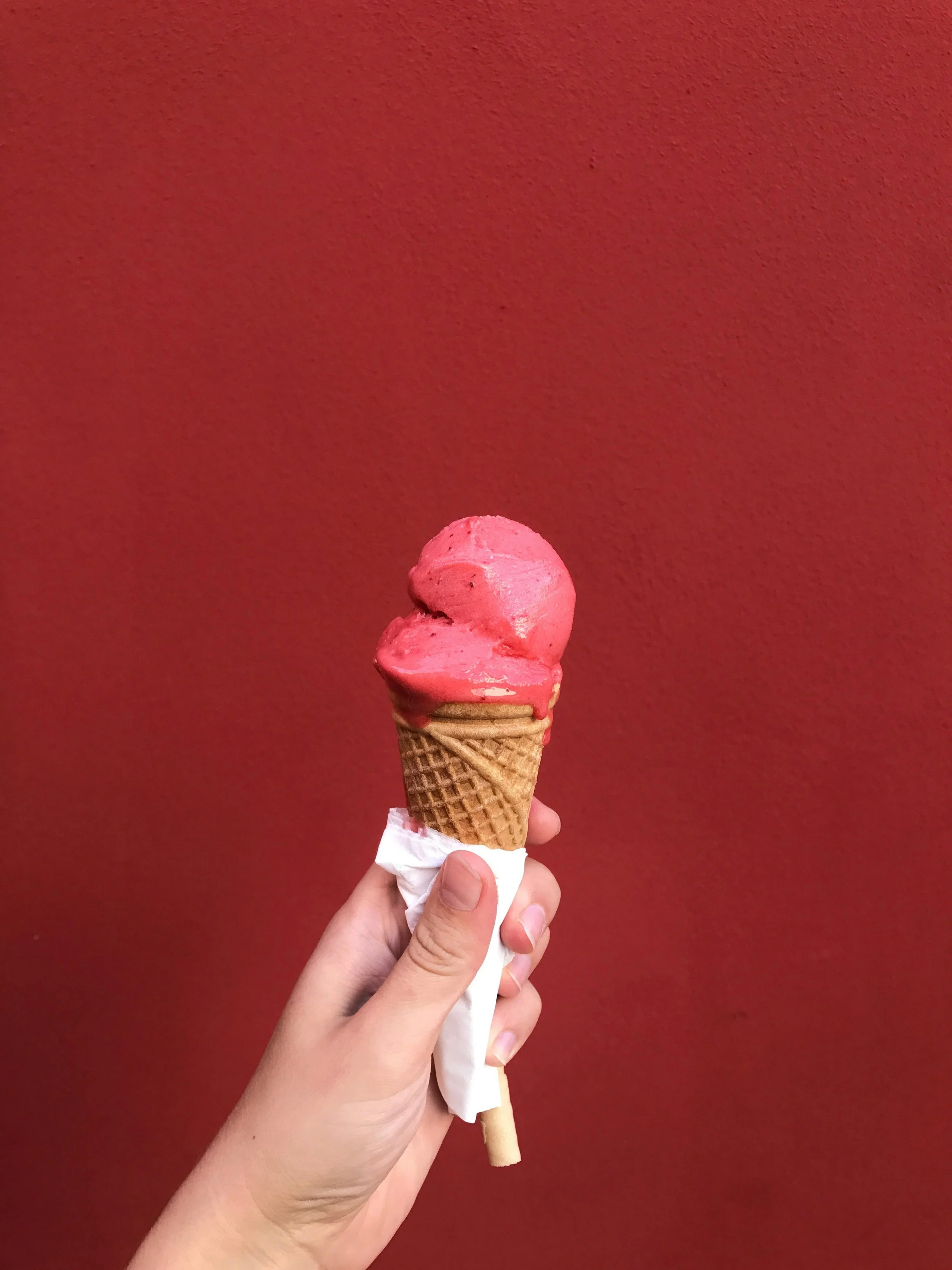 Hand holding strawberry ice cream against red wall