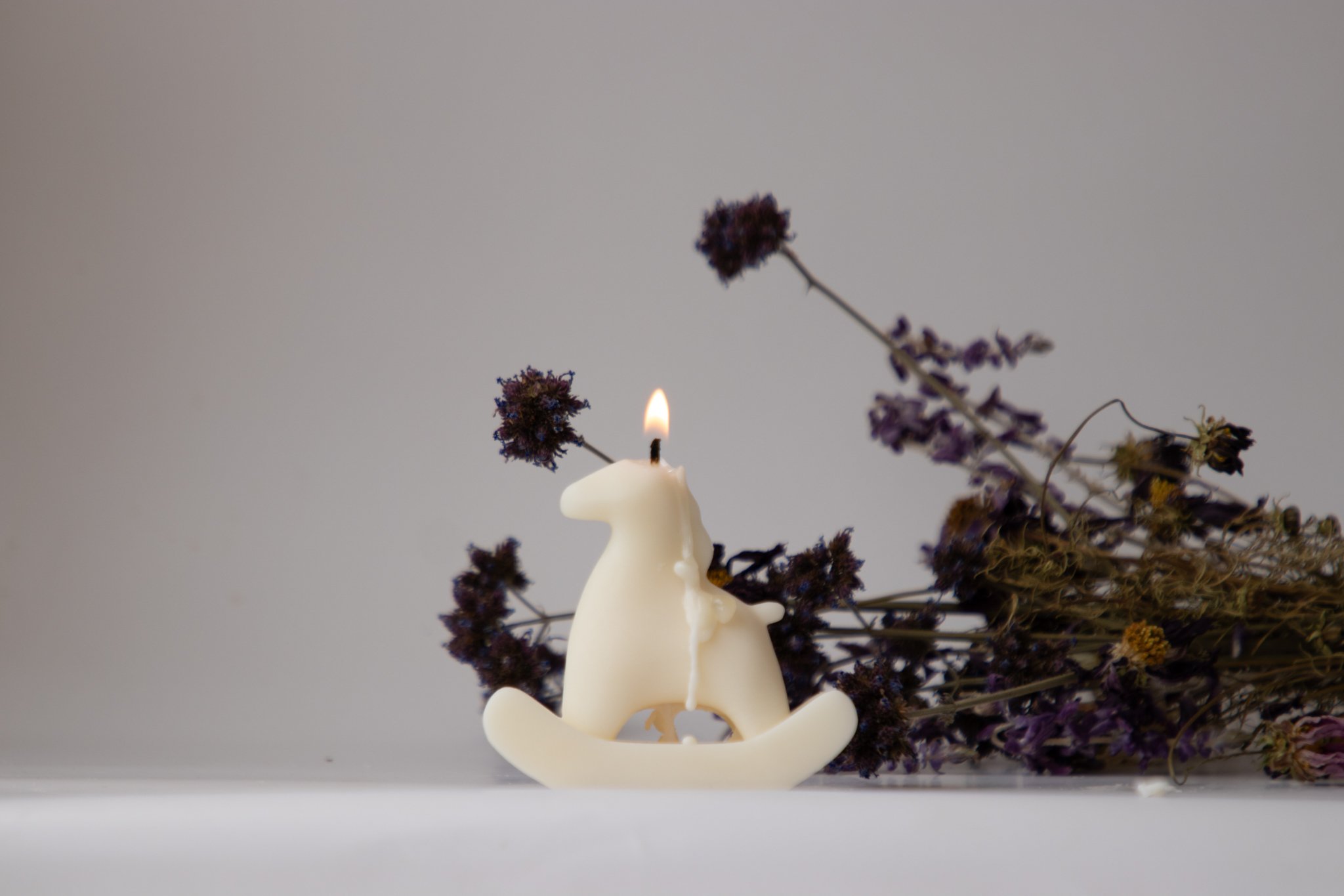 Lit rocking horse shaped soy candle with dripping wax, styled with dried purple flowers