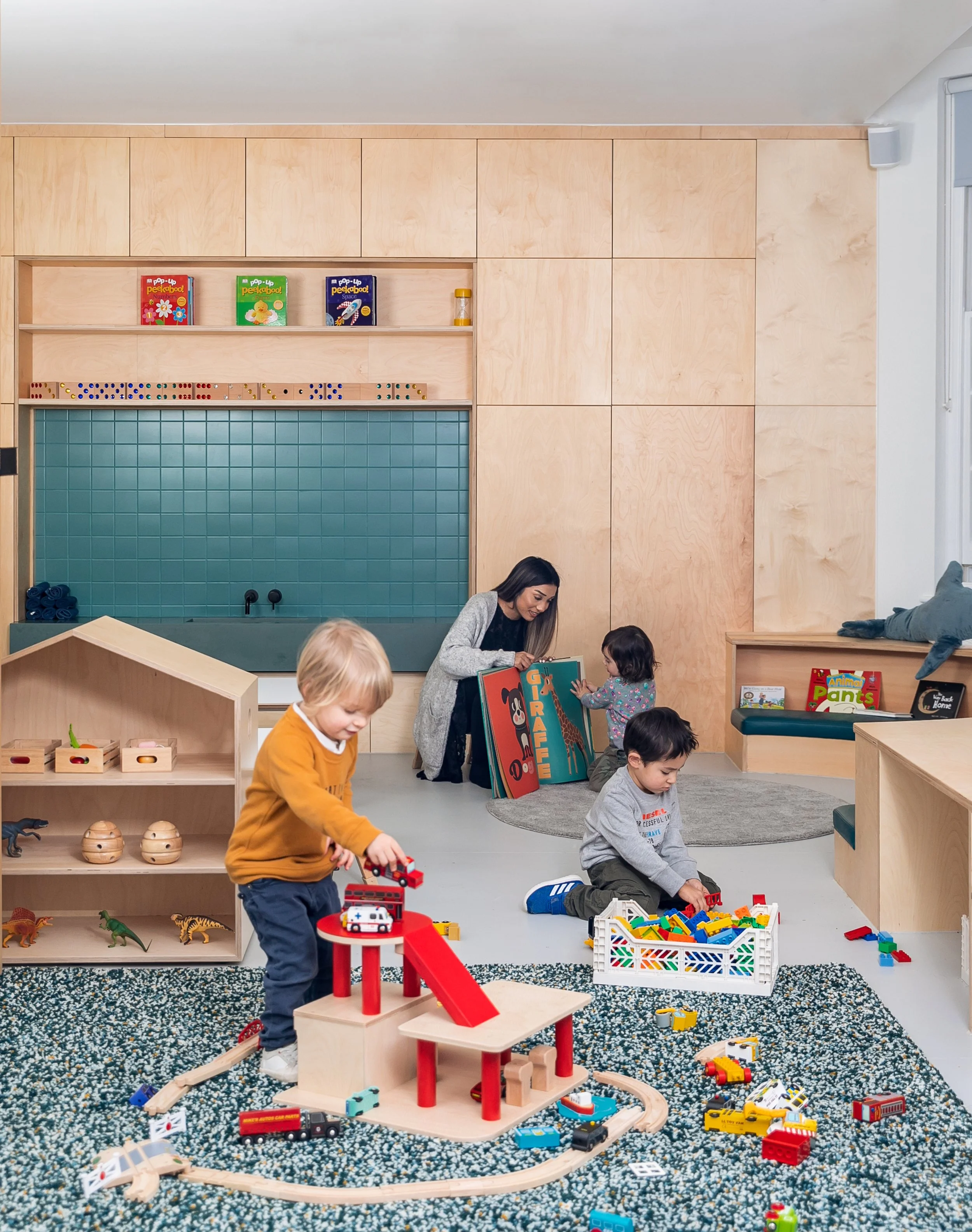 Children and teacher in an early years playroom with timber joinery, integrated seating, and open-ended play areas designed to support creative learning and child-centred education.