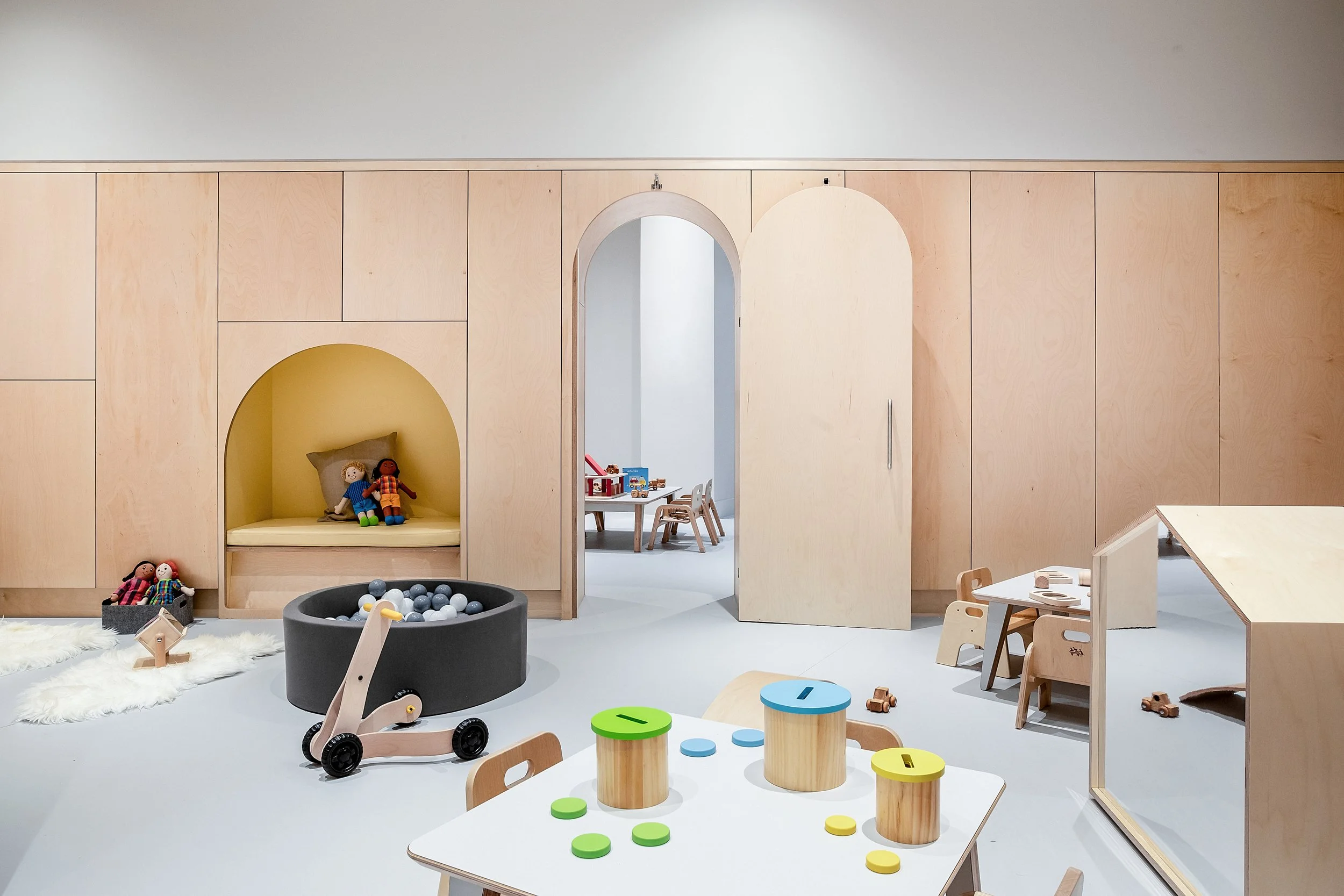 Contemporary early years playroom with integrated timber joinery, arched doorways, soft play areas, and child-scale furniture designed to support imaginative play and independent learning.