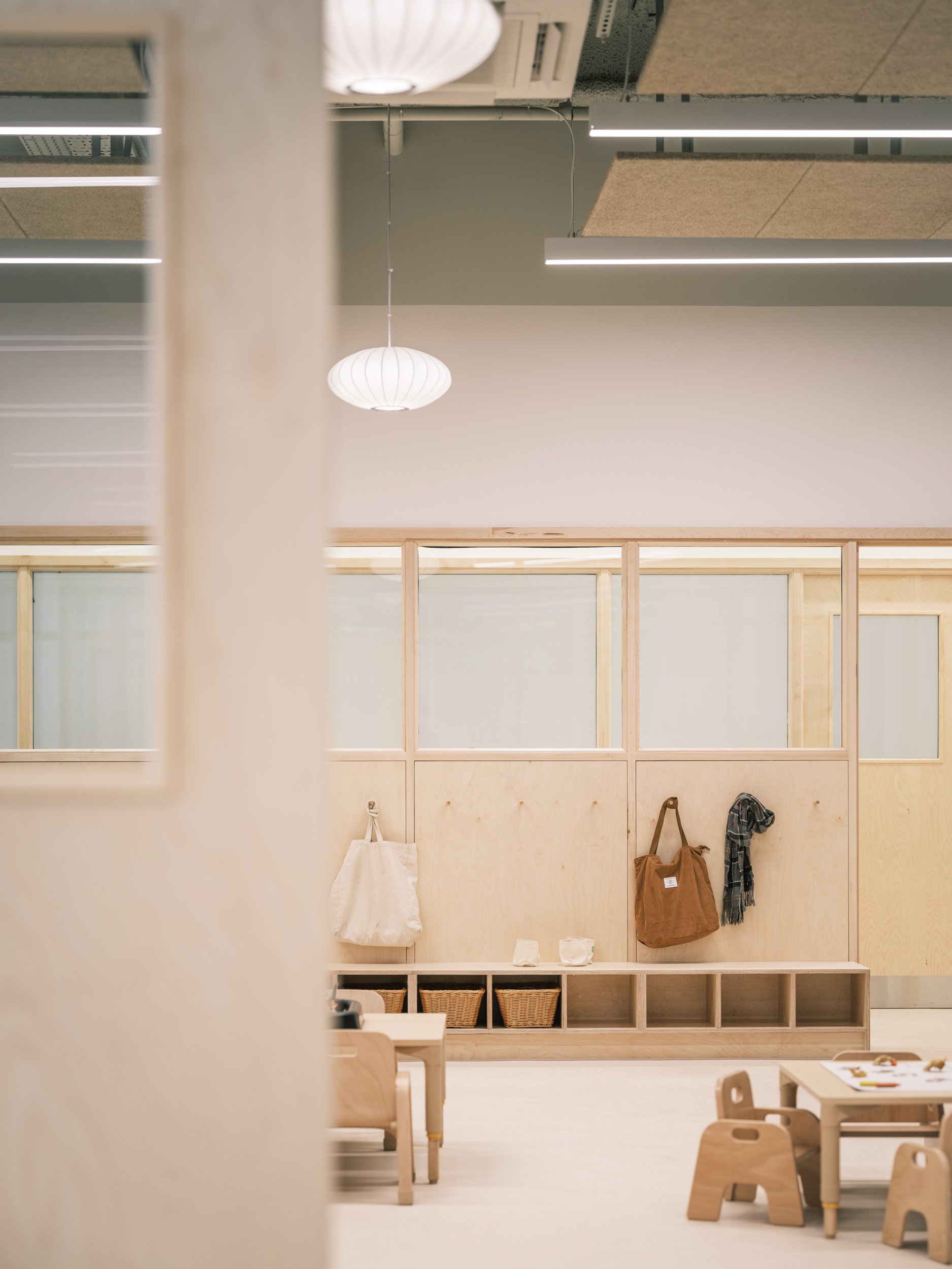 Modern early years classroom featuring integrated timber cloakroom storage, child-height cubbies, glazed partitions, woven baskets, and natural wood furniture designed to support independent learning and organised daily routines.