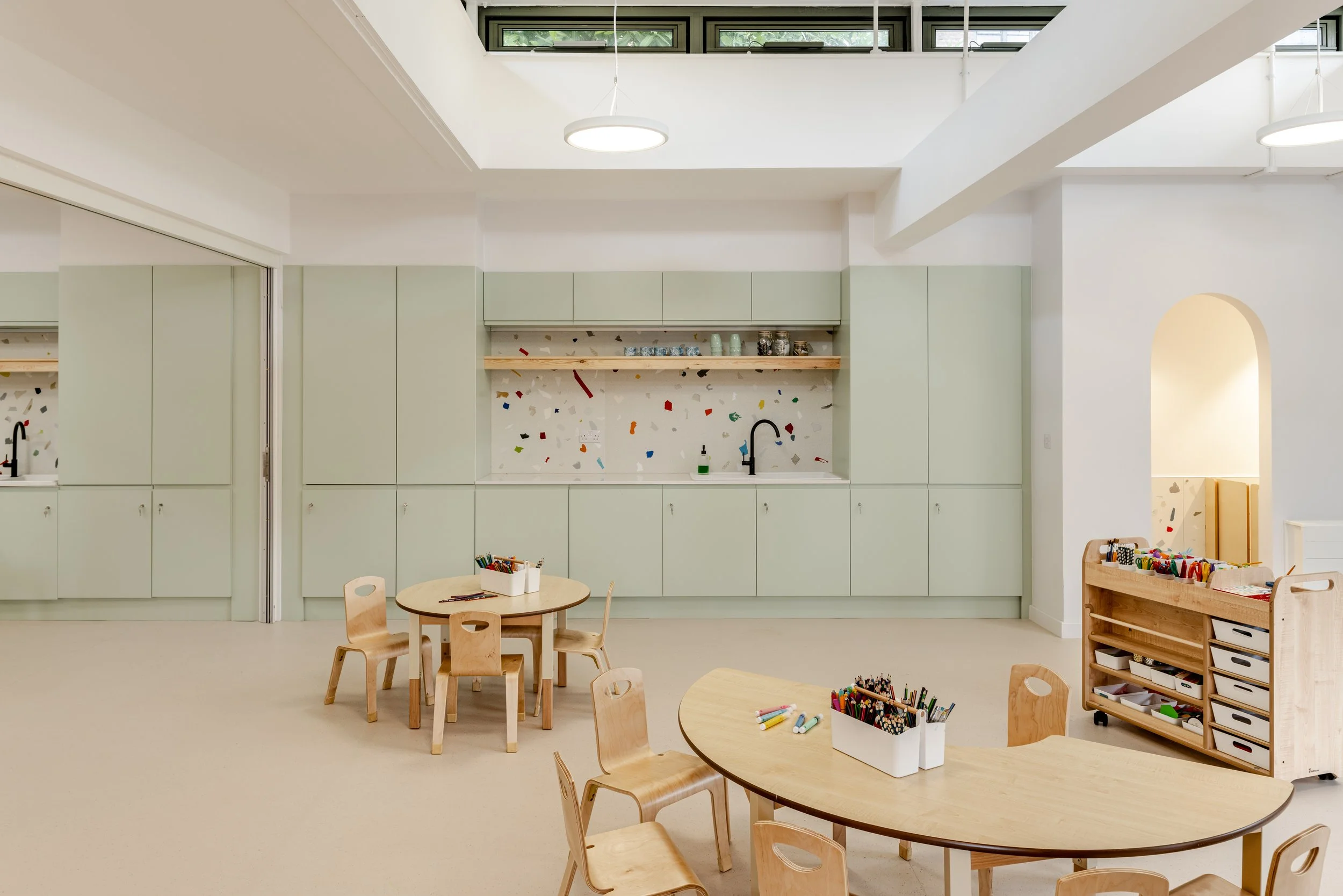 Bright early years classroom interior with pastel green storage walls, child-sized timber furniture, and terrazzo-style splashback designed for a calm and pupil-centred learning environment.