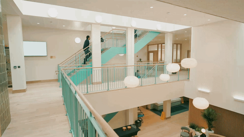 Interior of a modern building with a staircase and balcony area, featuring hanging pendant lights and minimalistic decor.
