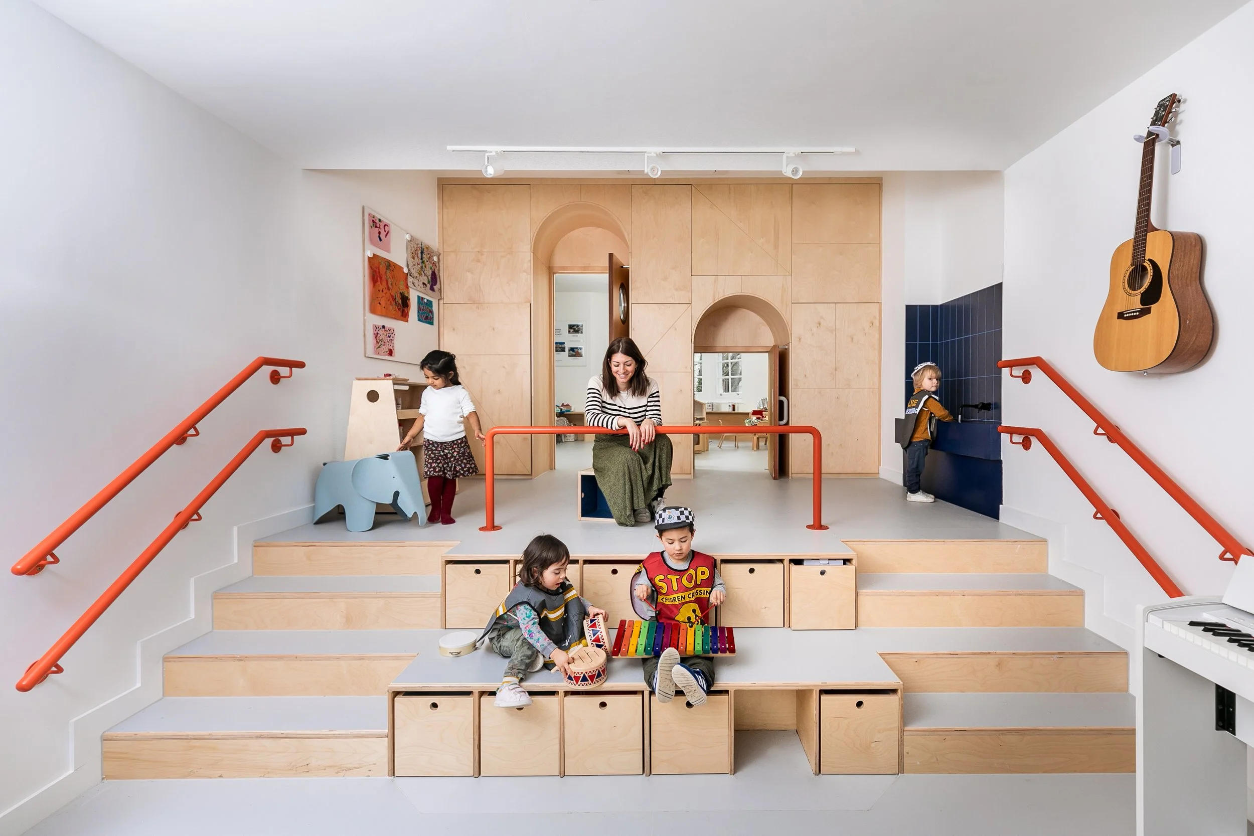Children and teacher in an early years playroom with timber joinery, integrated seating, and open-ended play areas designed to support creative learning and child-centred education.