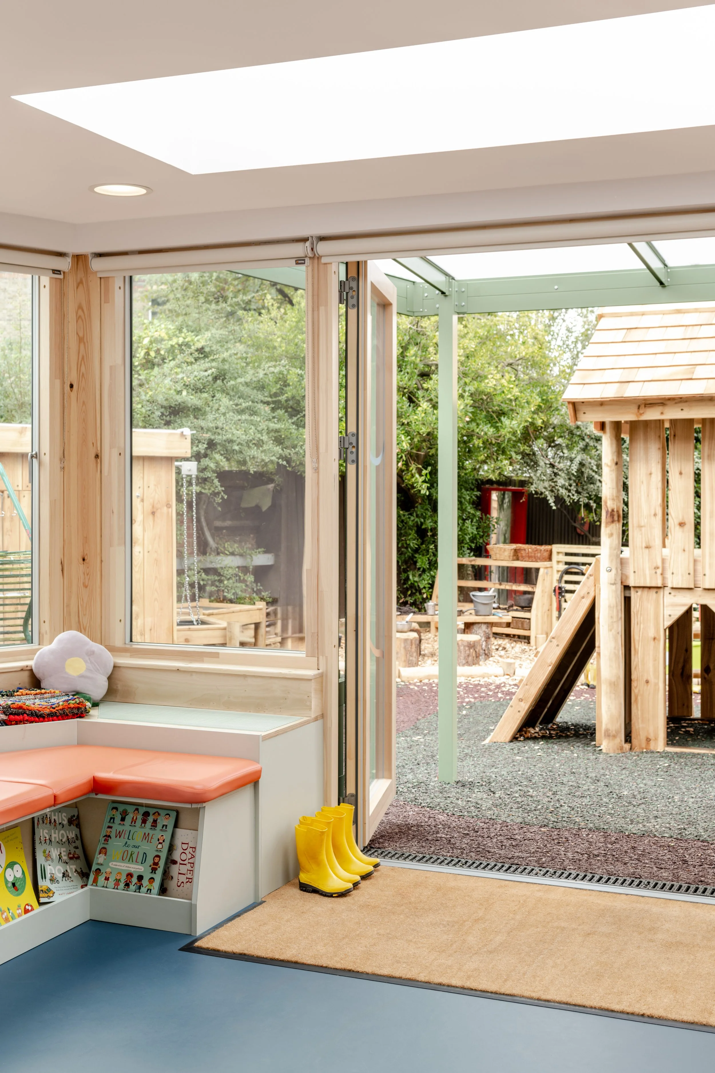 Early years classroom with timber-framed glazing and direct access to an outdoor play area featuring natural timber play equipment and covered learning spaces.