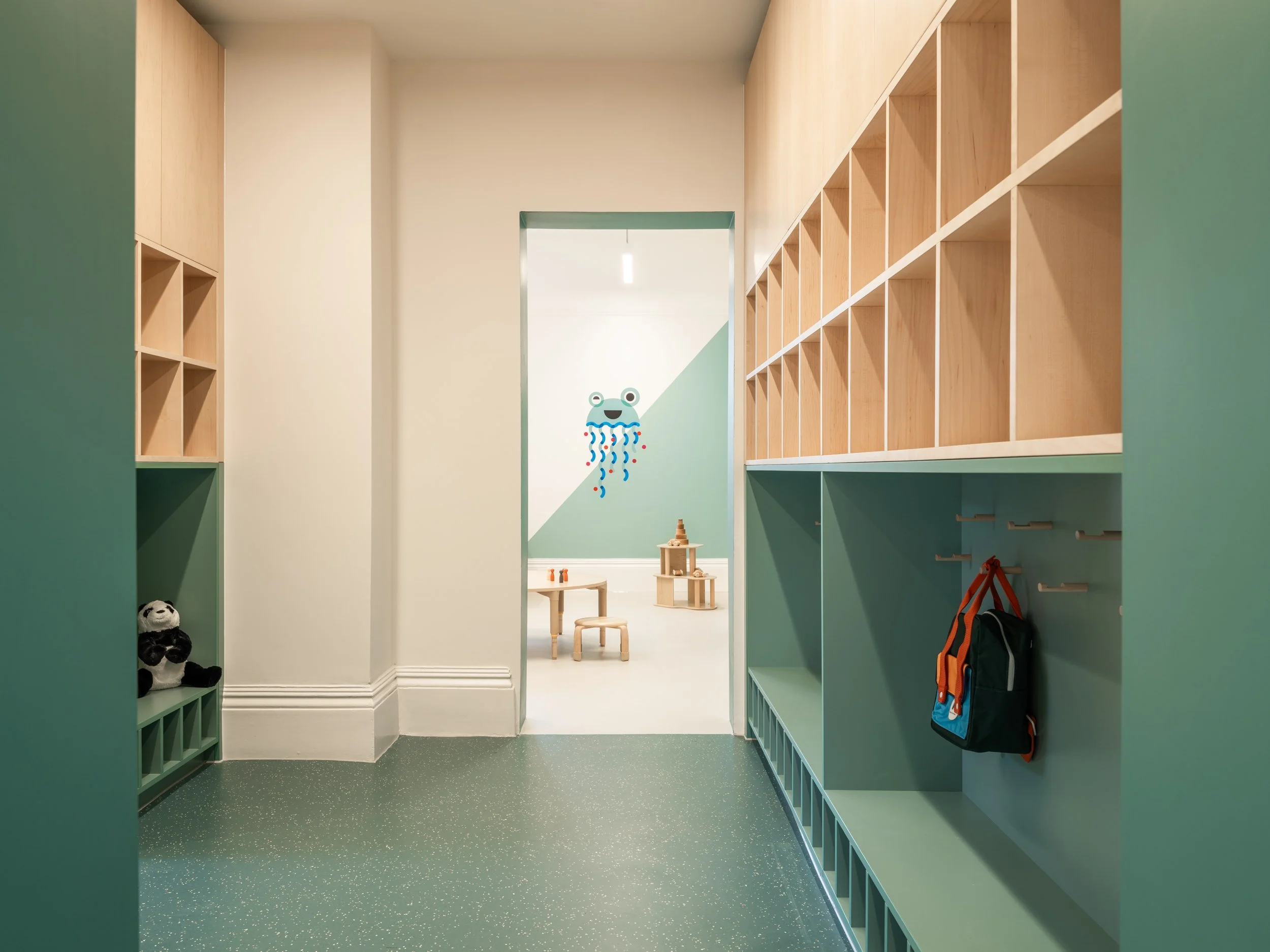 Early years cloakroom with integrated timber storage, pastel green joinery, and child-scaled furniture designed to support independence, organisation, and welcoming learning environments.
